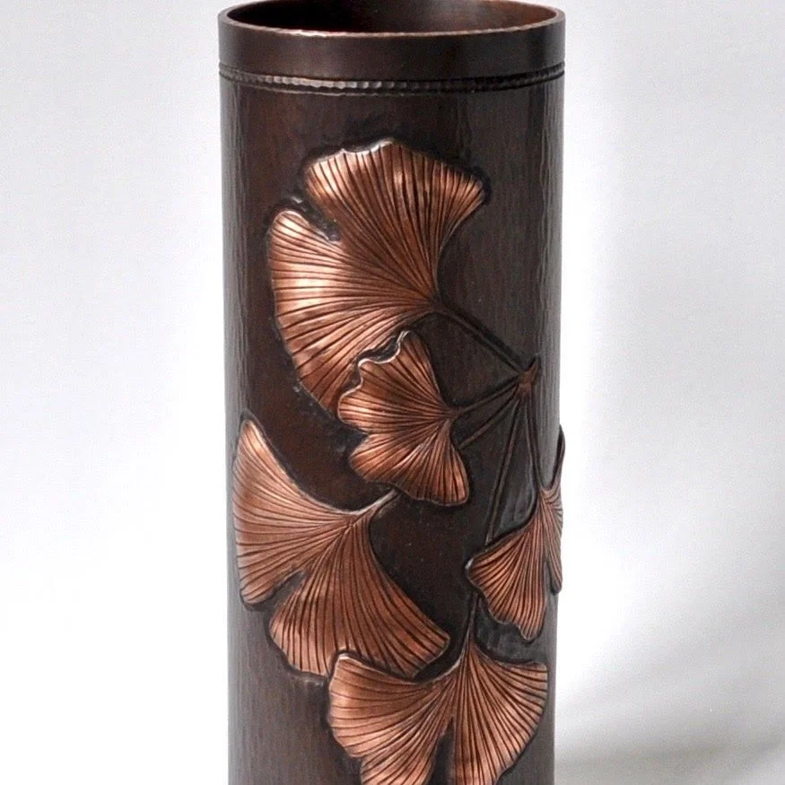 Artist: Anne Jordan. 
https://www.annejordancopperwork.com/vessels 

This ginkgo vase is made from copper and has a liver of sulfur patina. The leaves have been pushed out from the inside to create relief. It has a subtle hammered background texture.