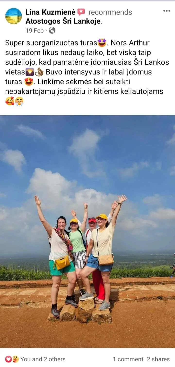 Four women standing on rocks outdoors, smiling and waving. They are on a hill with a scenic view of the sky and landscape behind them, wearing casual clothes and hats.