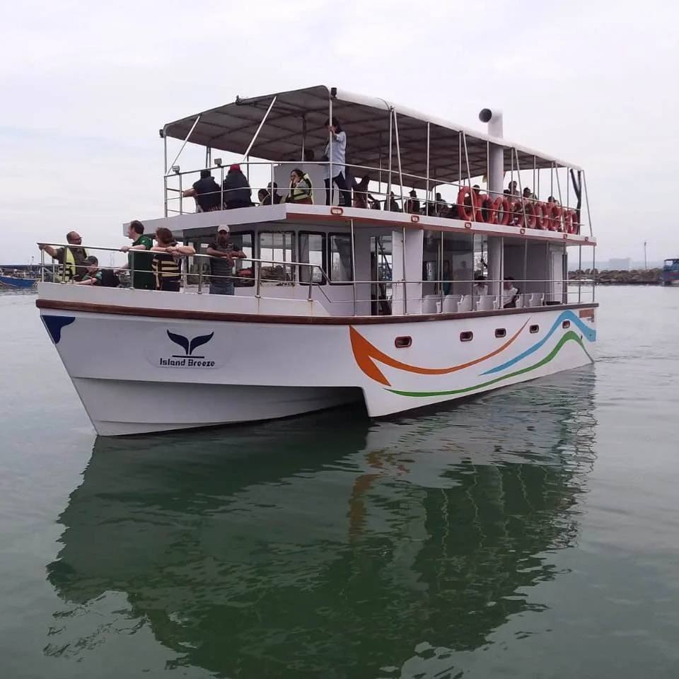 Passenger boat named Island Breeze on the water with people on board, some standing at the railing, others sitting under a canopy.