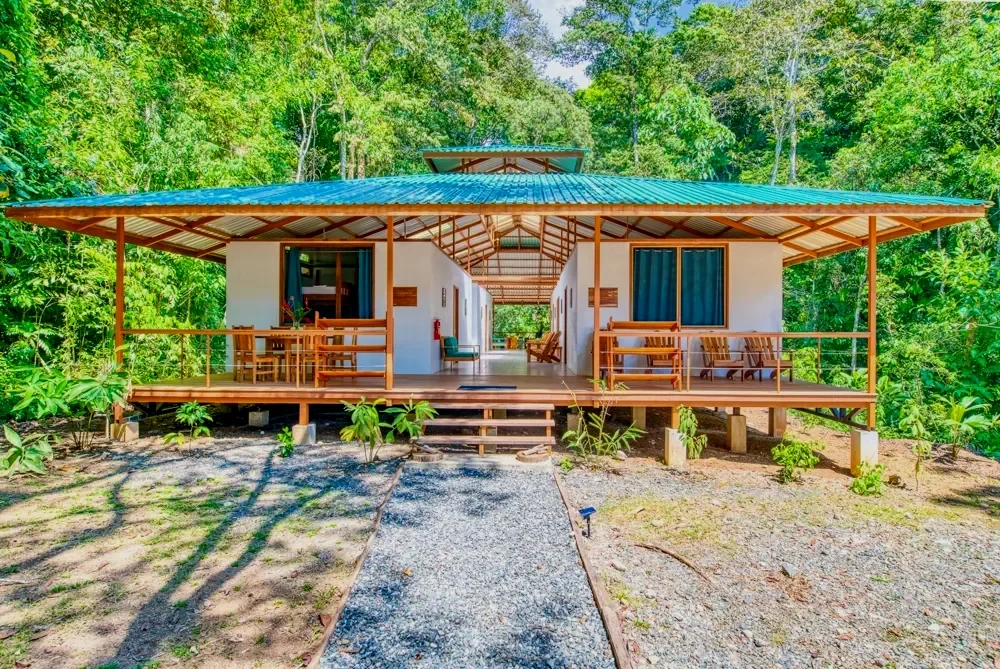 A single-story house with a large front porch surrounded by lush green trees.