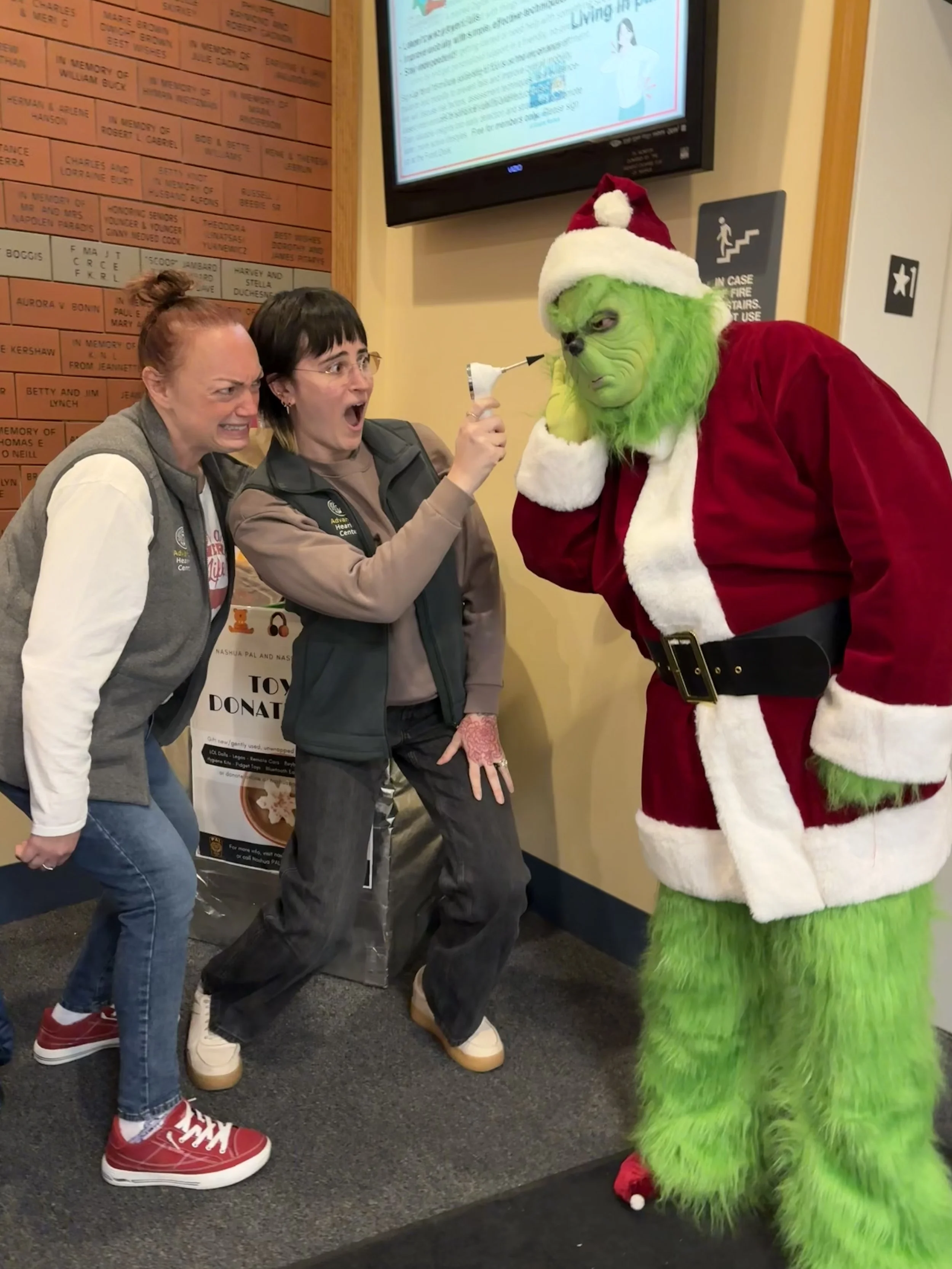Dr. Emma Michaud, audiologist and Erin Blassberg, Hearing Instrument Specialist looking in the Grinch's ear