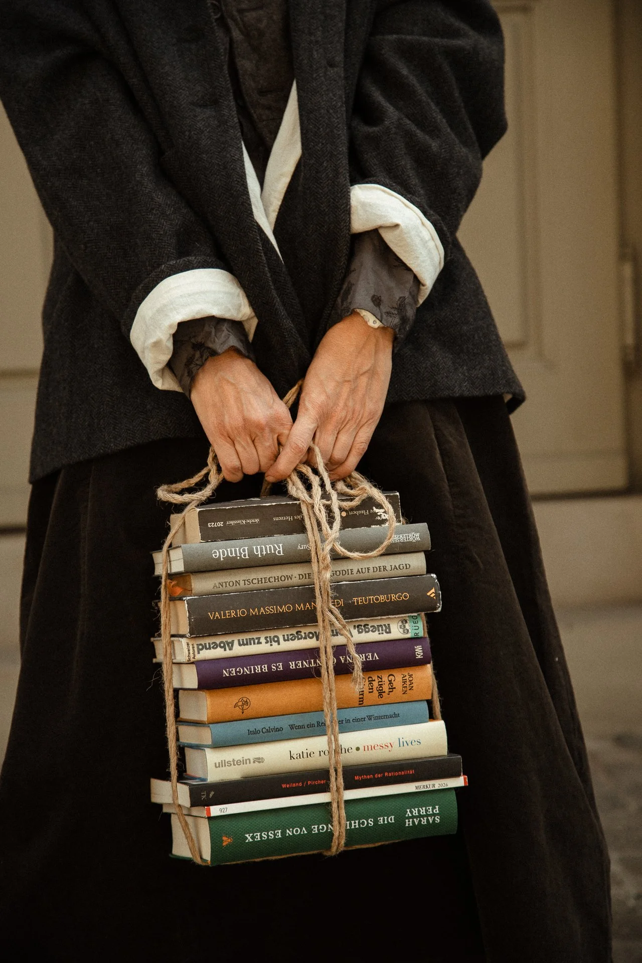 Person wearing a dark coat with rolled-up sleeves holding a stack of books tied with string.
