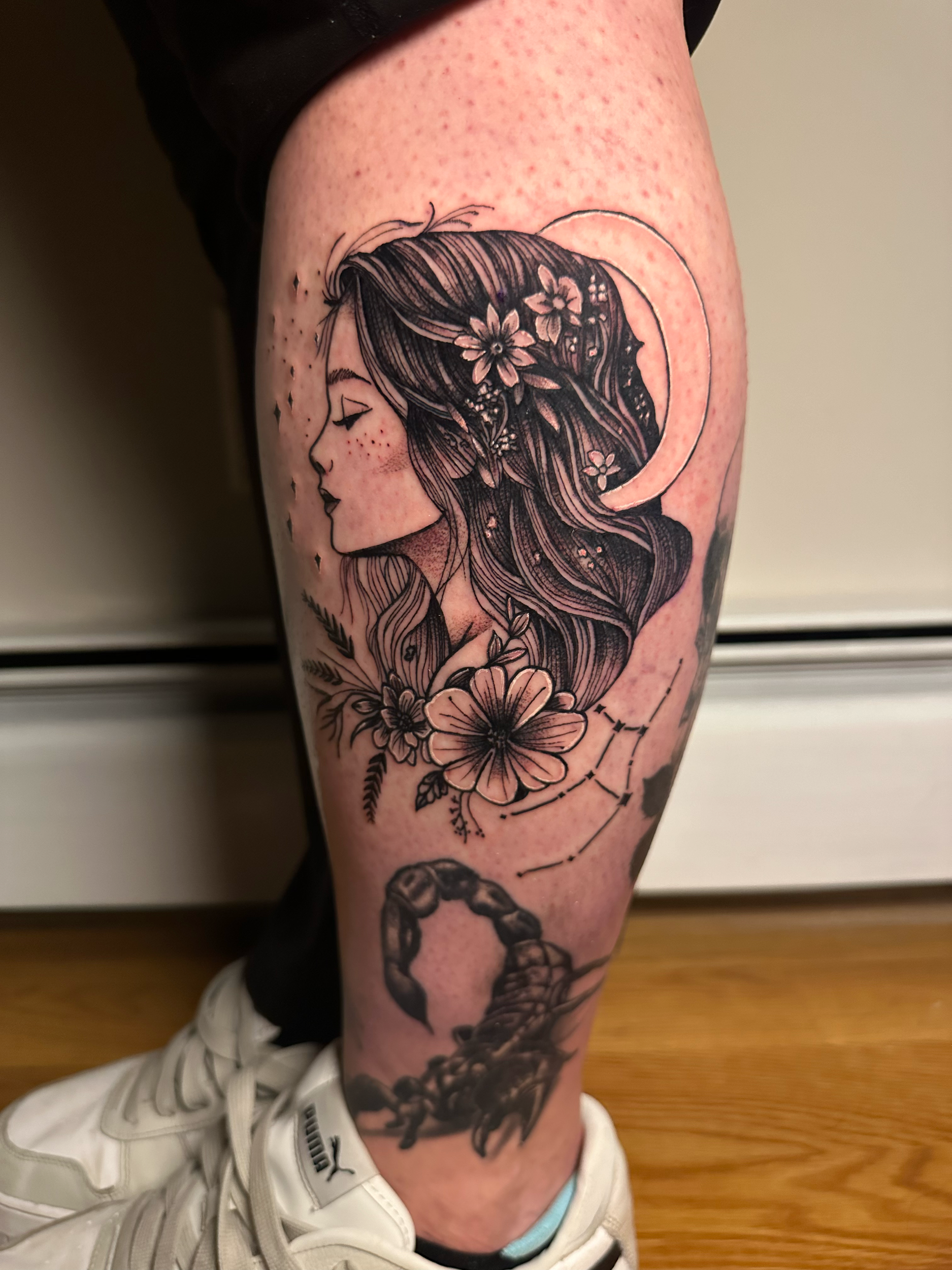 Tattoo on a person's leg depicting a side profile of a woman with floral hair and a scorpion.