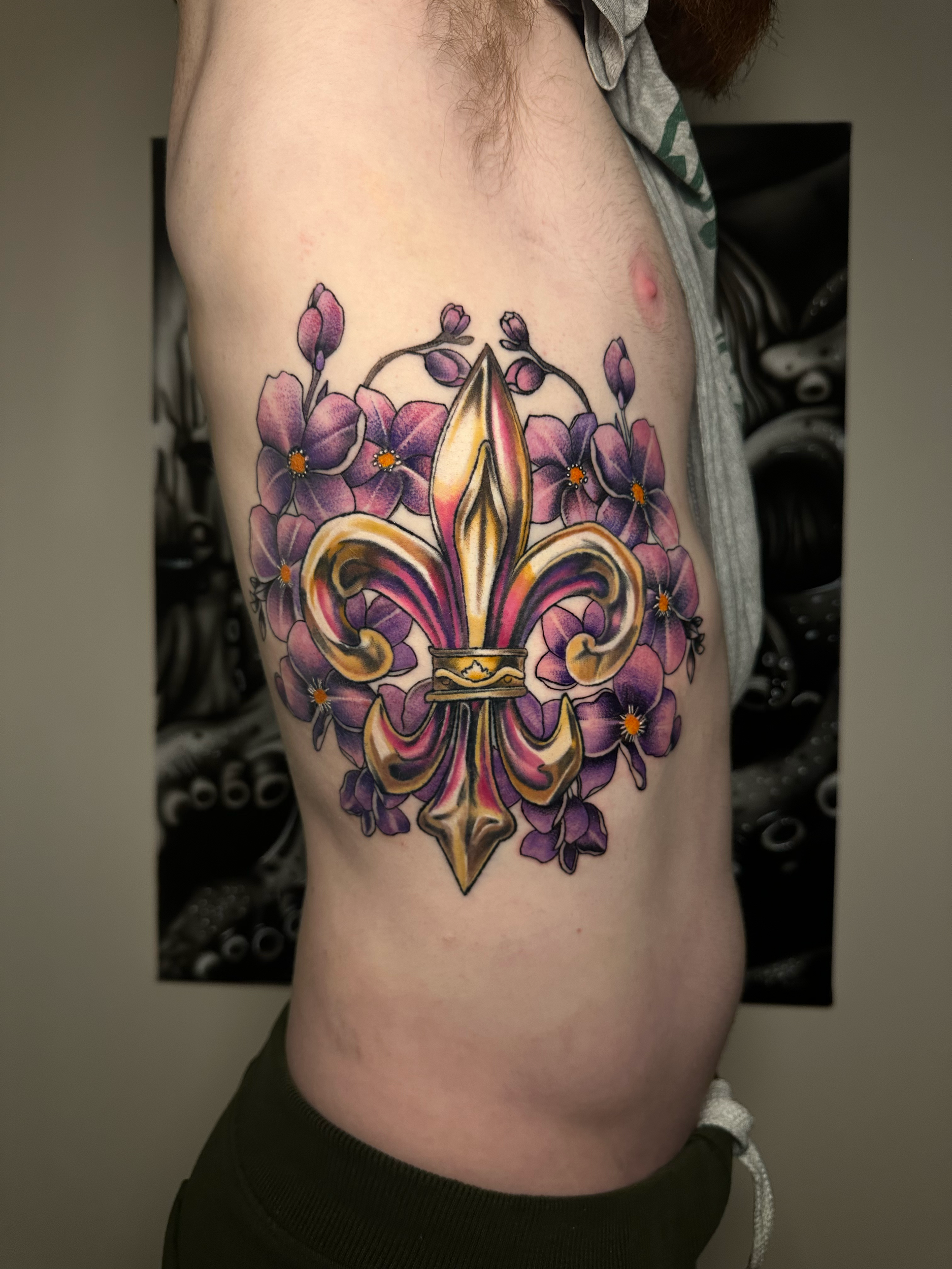 Colorful tattoo of a fleur-de-lis with purple flowers on a person's ribcage.