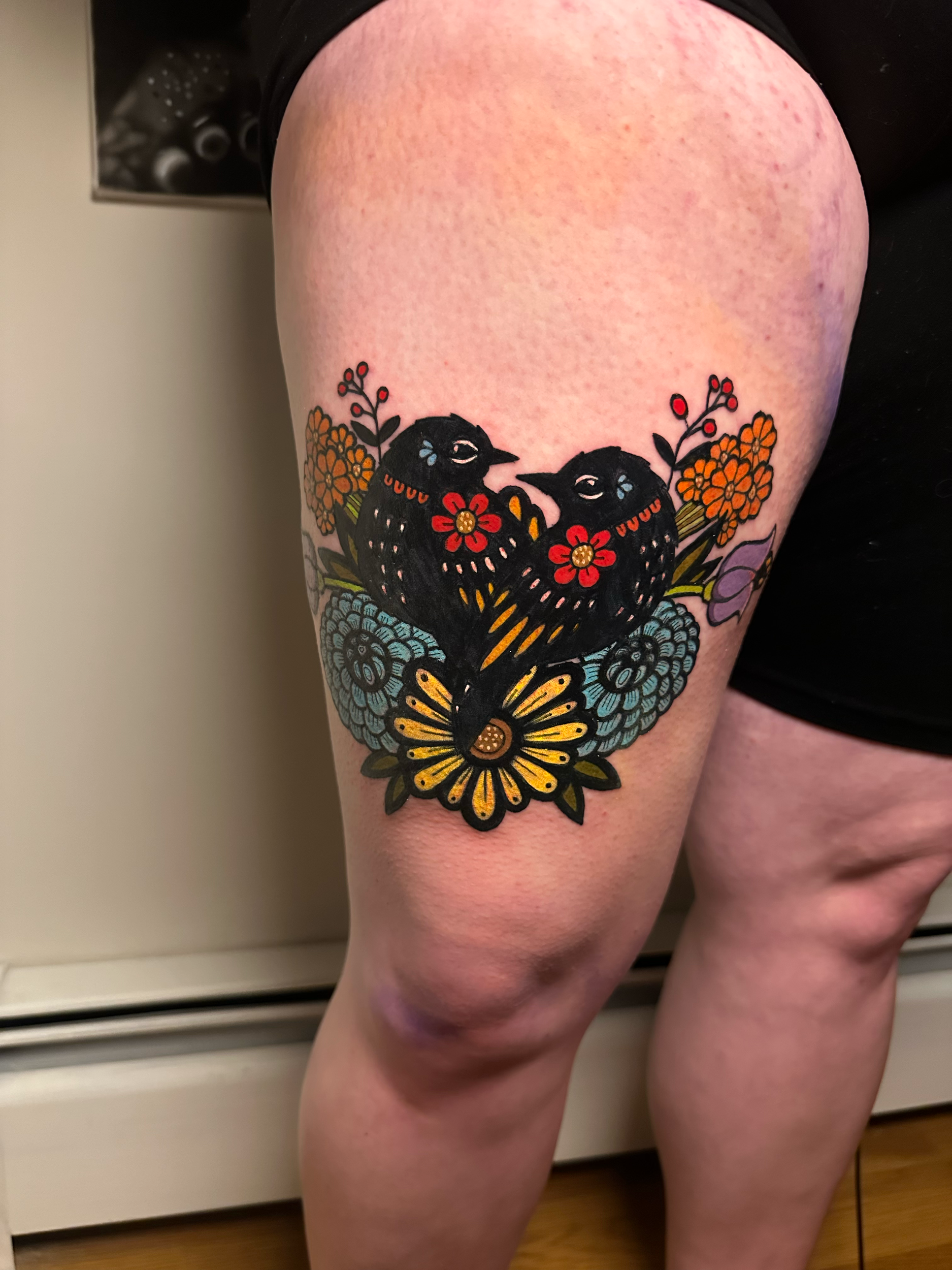 Tattoo of stylized birds and flowers on thigh