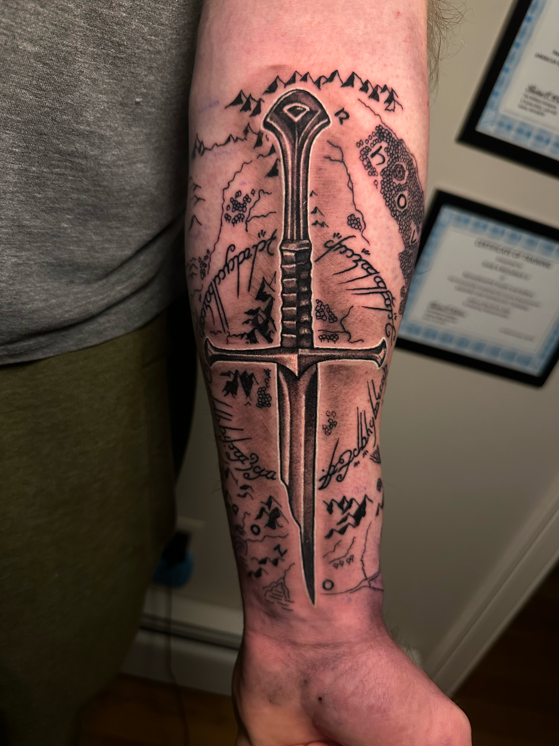 Tattoo of a dagger with Elvish script and Middle-earth map on forearm