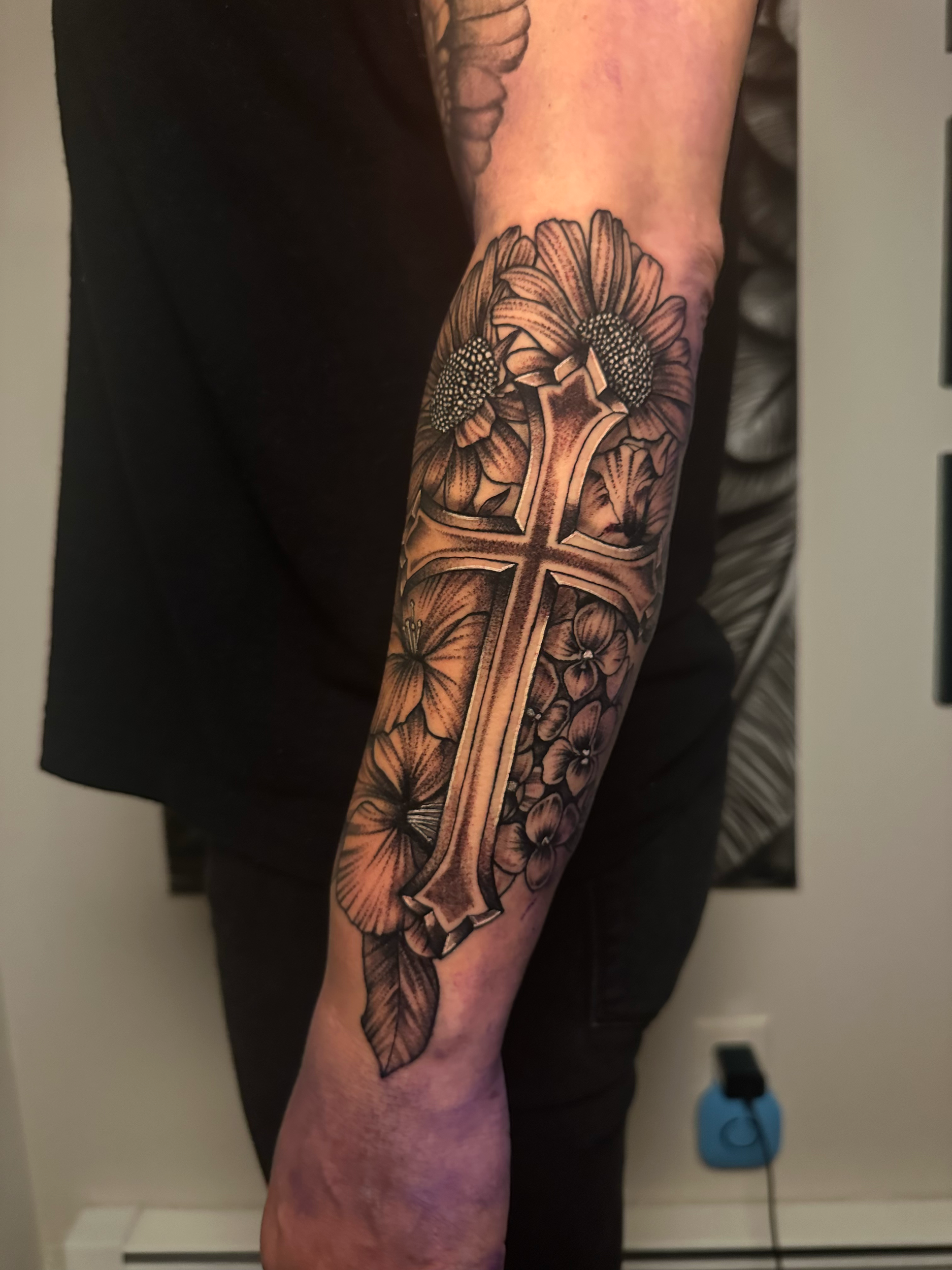 A tattoo of a cross surrounded by flowers on a person's forearm.