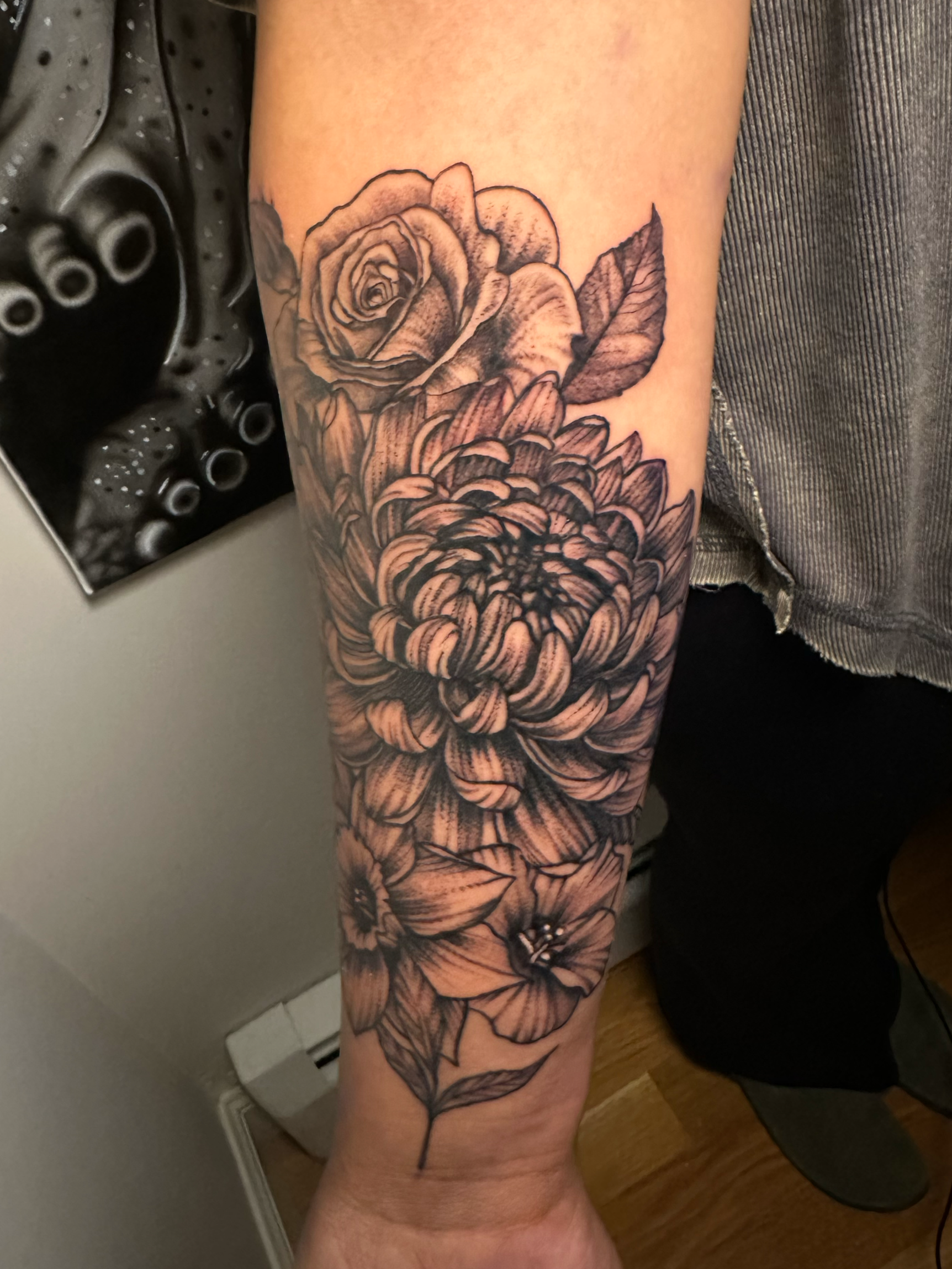 Forearm tattoo featuring detailed black and gray floral design with chrysanthemums and roses.