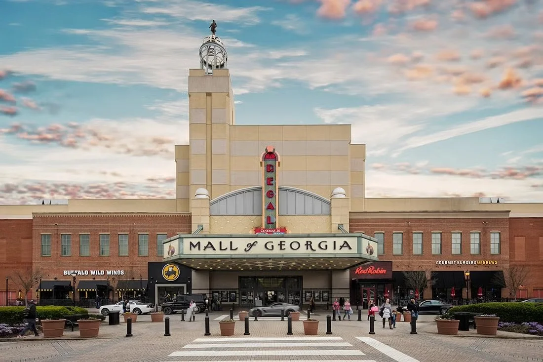 Facade of Mall of Georgia with a large marquee sign, a vertical Regal theater sign, and various storefronts including Buffalo Wild Wings and Red Robin, with people walking in front.