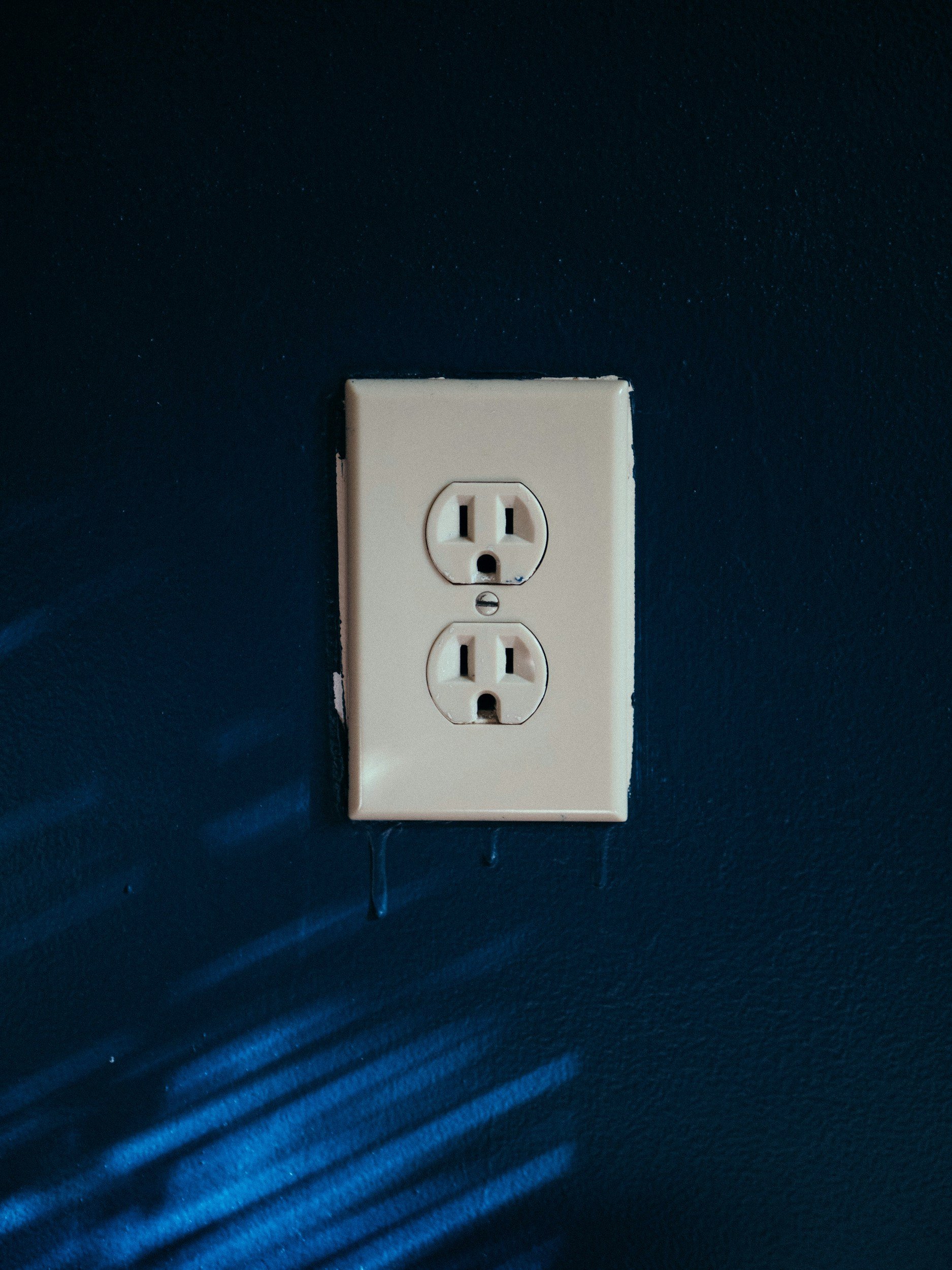 A white electrical outlet with two sockets on a blue wall.