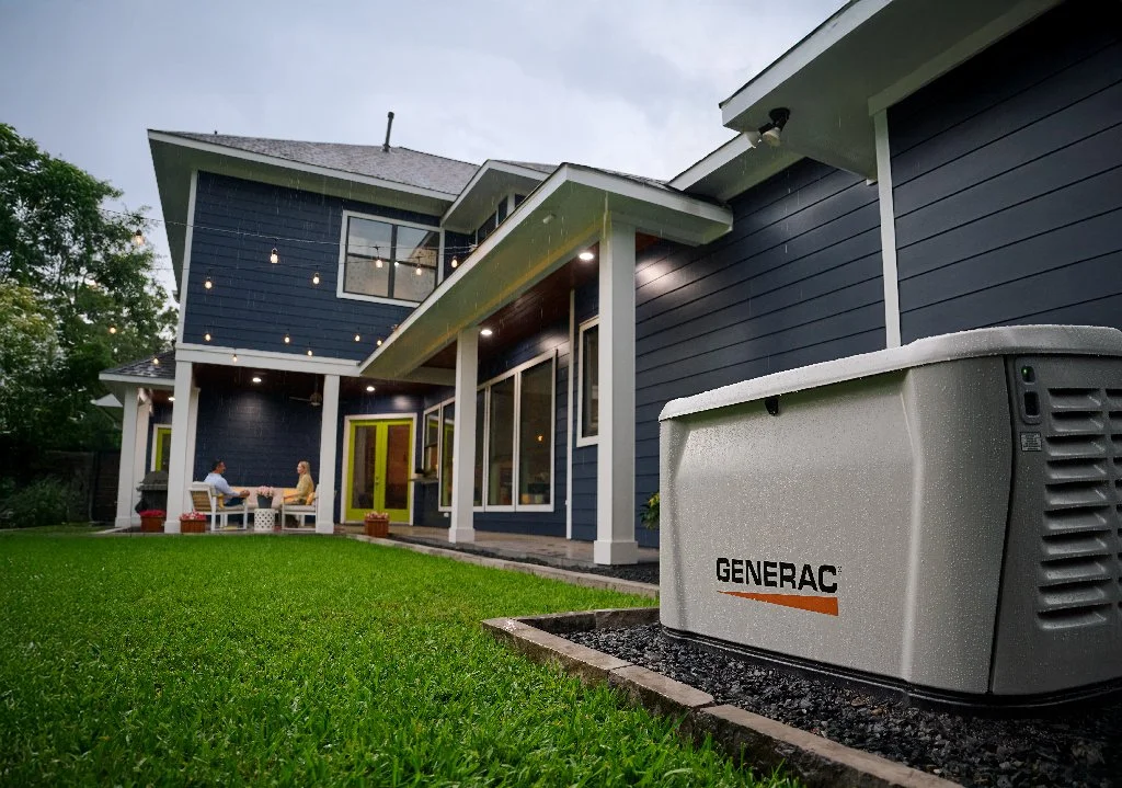 A modern two-story house with a backyard, a lawn, and a Generac generator outside. Two people are sitting on benches on the patio, enjoying the outdoor space.