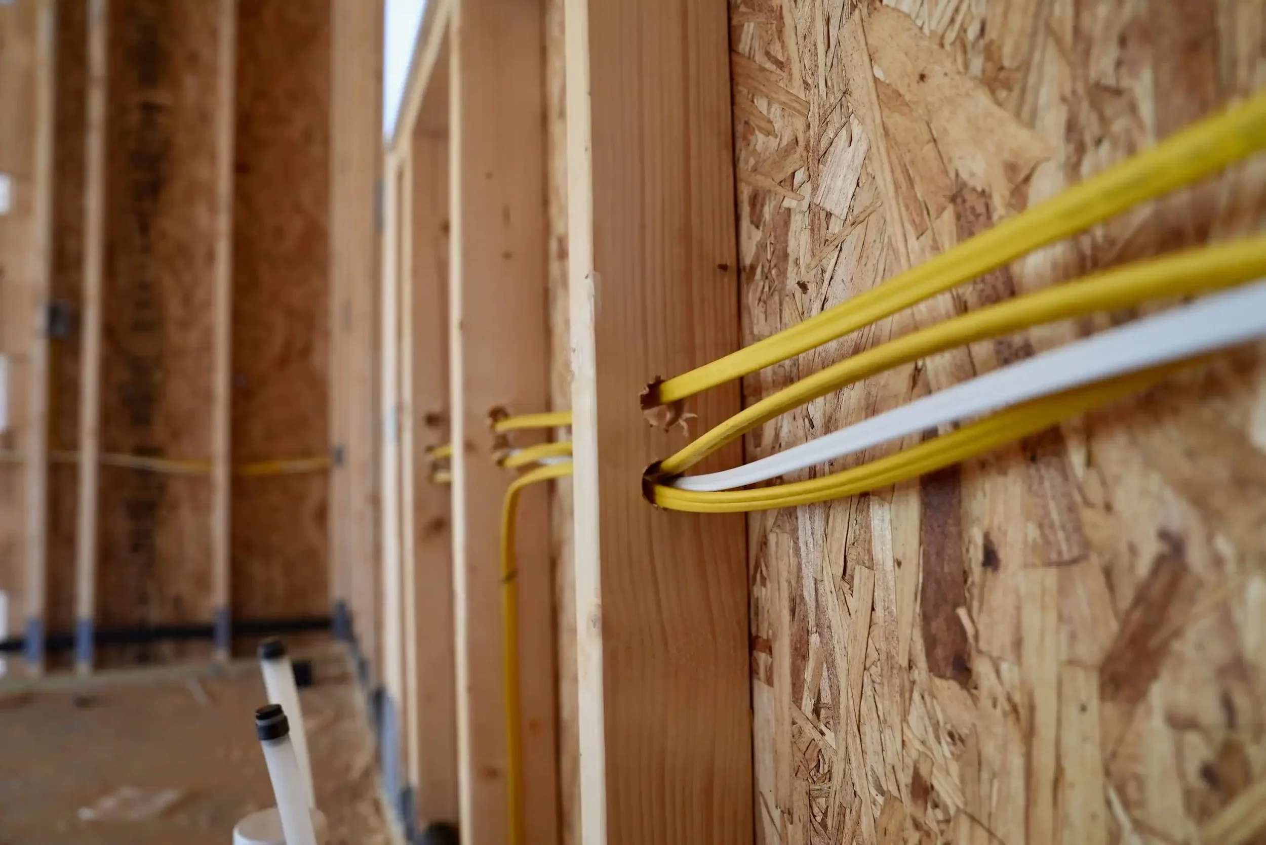 Close-up of electrical wiring installed along wooden wall studs in a construction site.