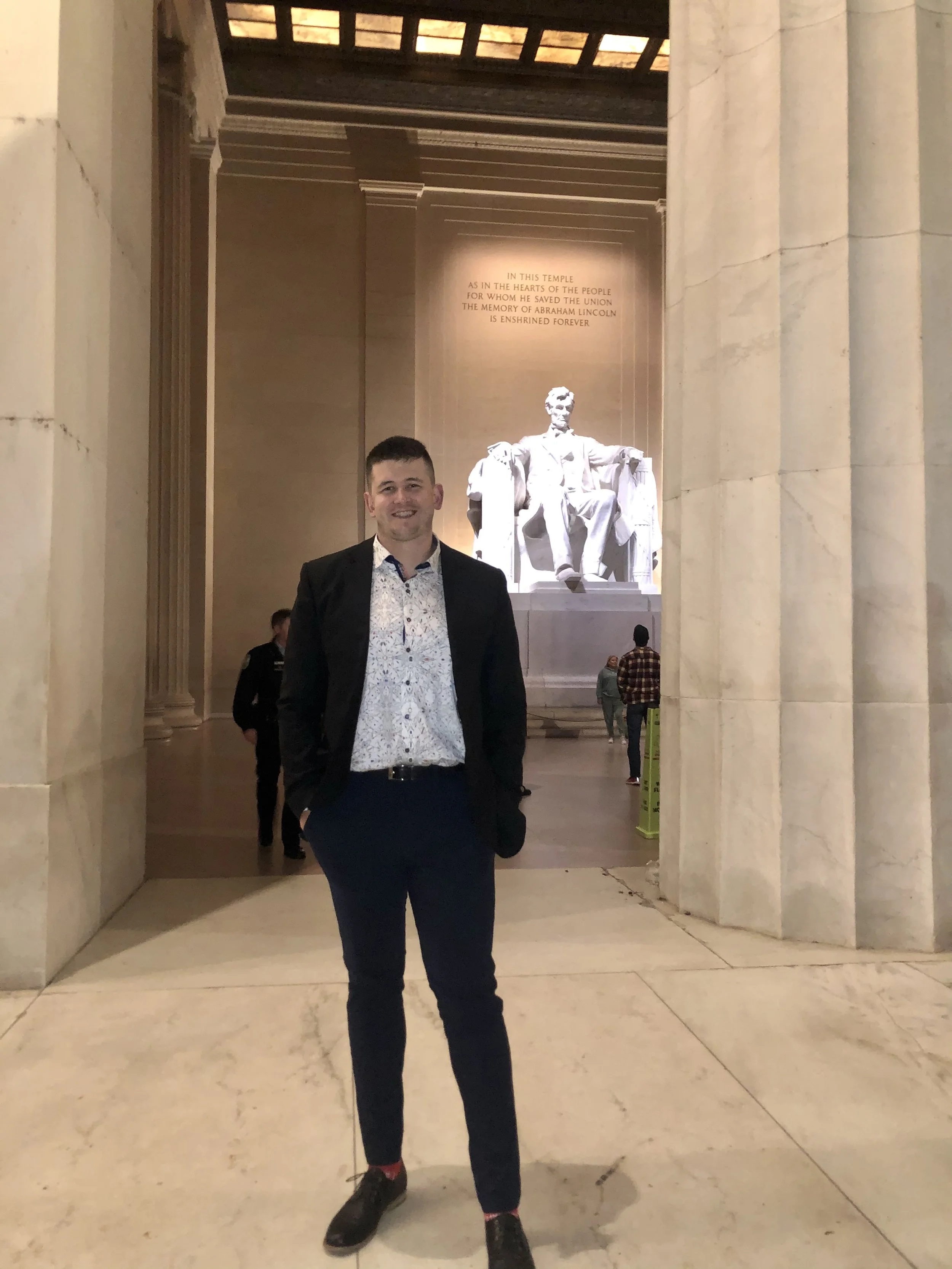 Ken King in a business suit smiling at the camera inside the Lincoln Memorial, with the statue of Abraham Lincoln visible in the background.