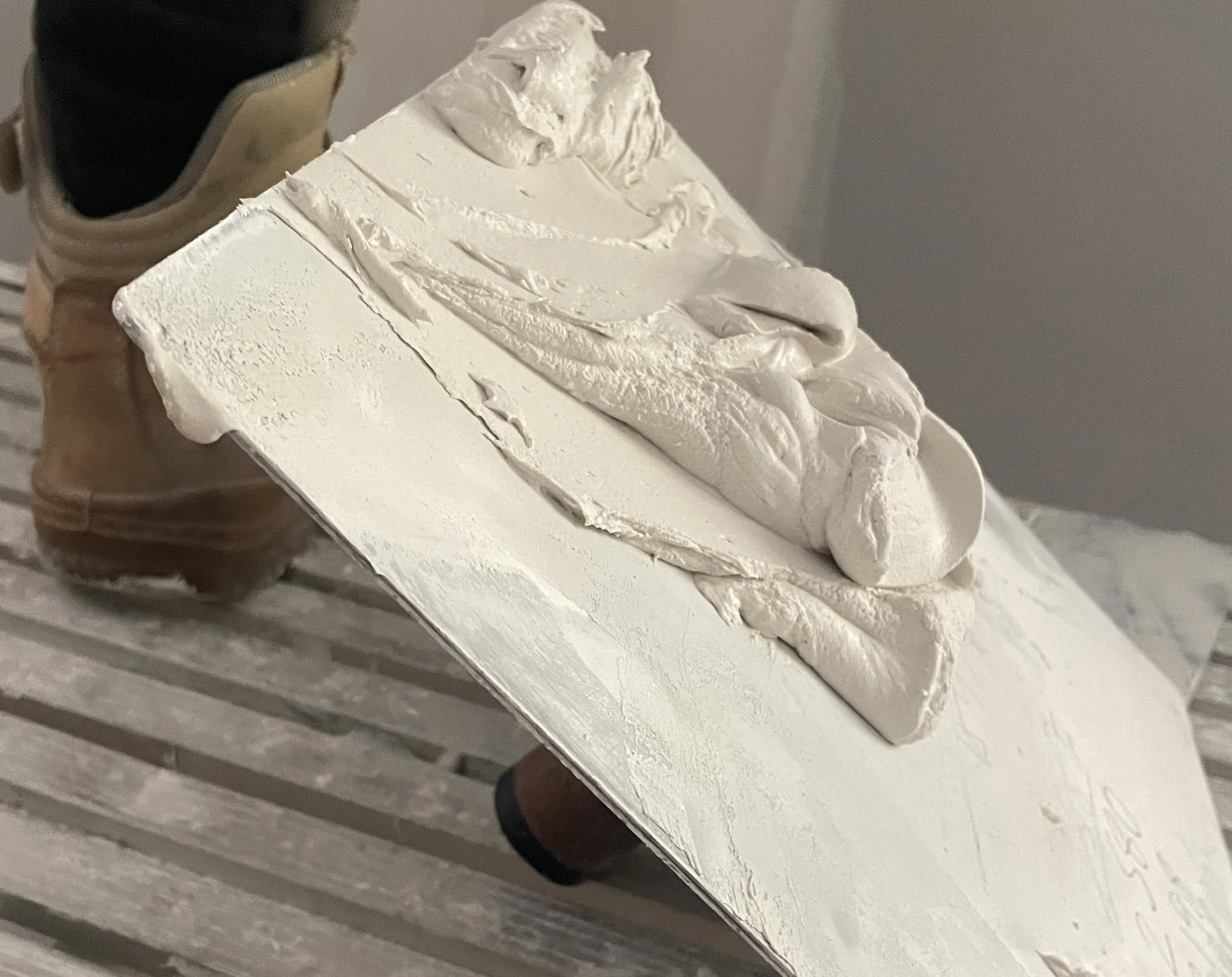 A white sculpture of a shoe and a foot on rectangular base with a sneaker in the background.