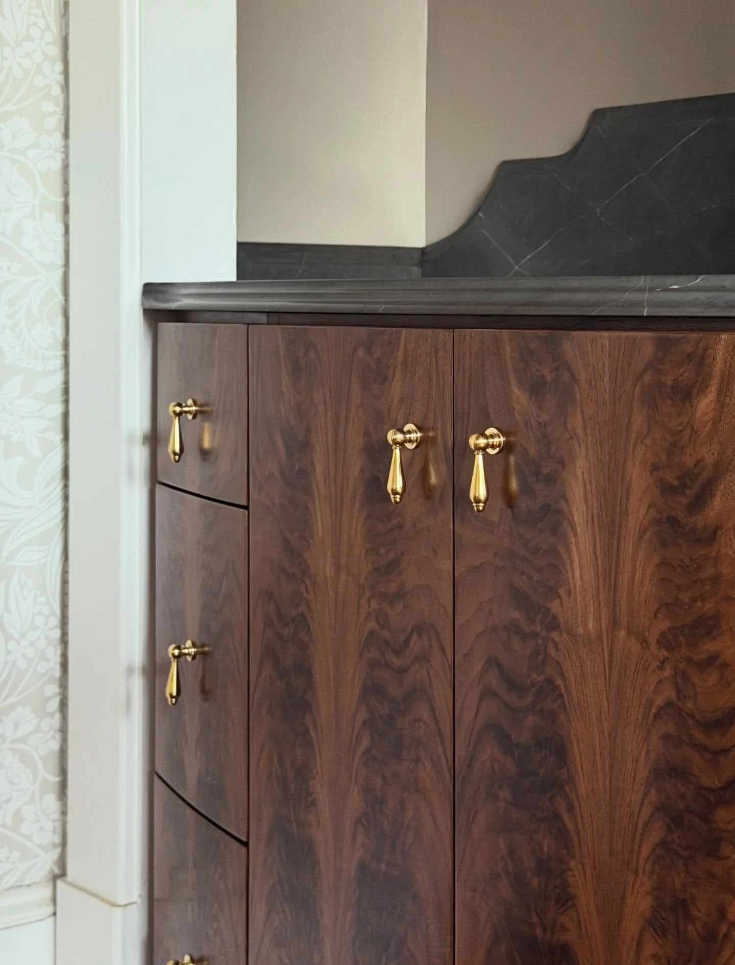 The craftsmanship showcased in these custom-built bar cabinets is truly exceptional. Bowed fiddleback walnut millwork highlights the natural beauty and movement of the wood, while unlacquered brass hardware adds a warm, timeless patina that will only