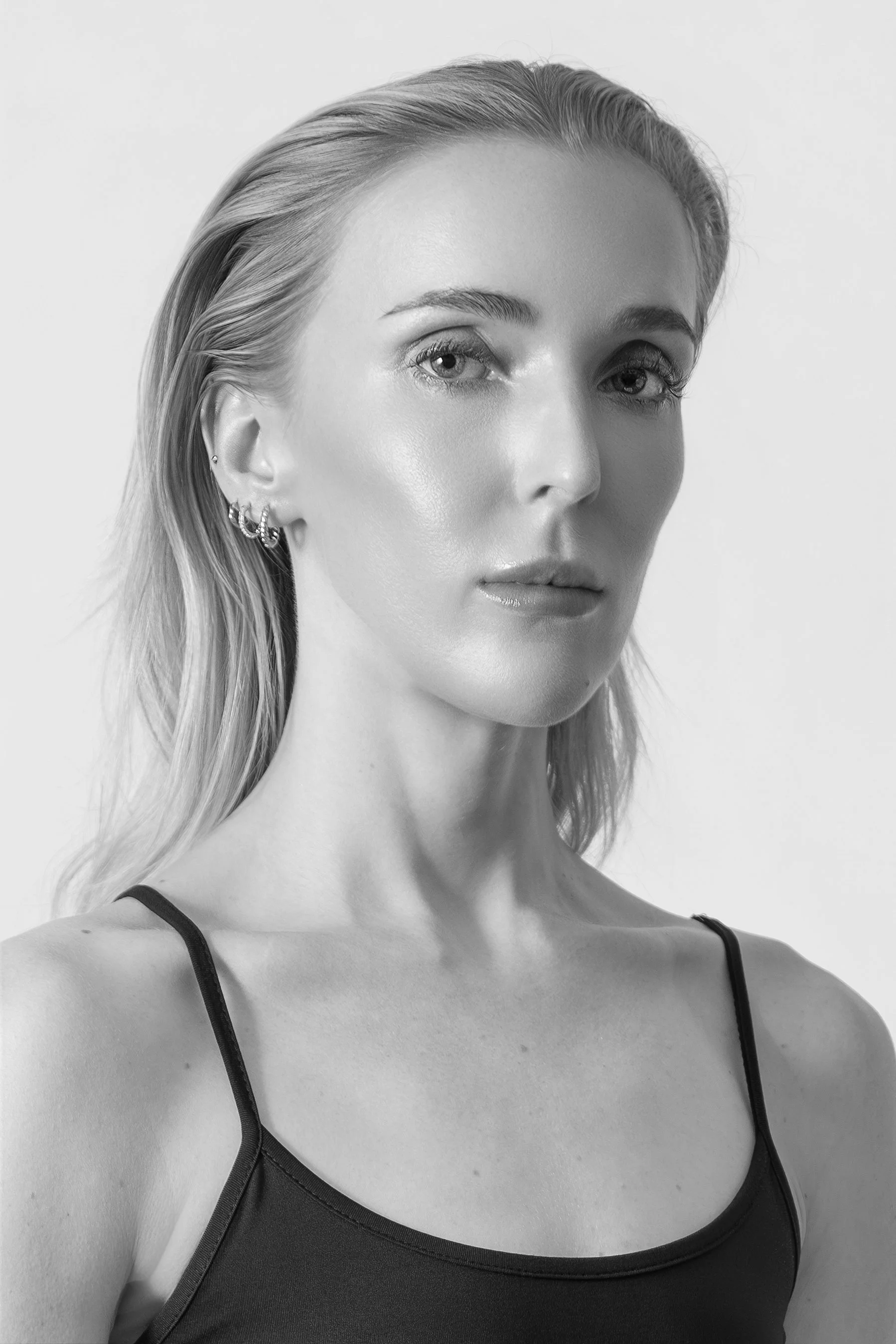 Black and white portrait of a woman with long hair, wearing a spaghetti strap top, looking at the camera with a neutral expression.