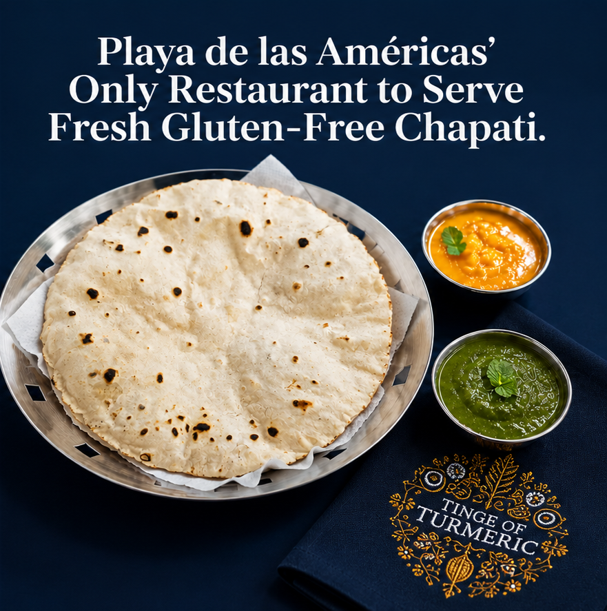 A basket of fresh chapatis with two small bowls of chutneys, one mango and one green, on a dark blue tablecloth with embroidered turmeric flower design.