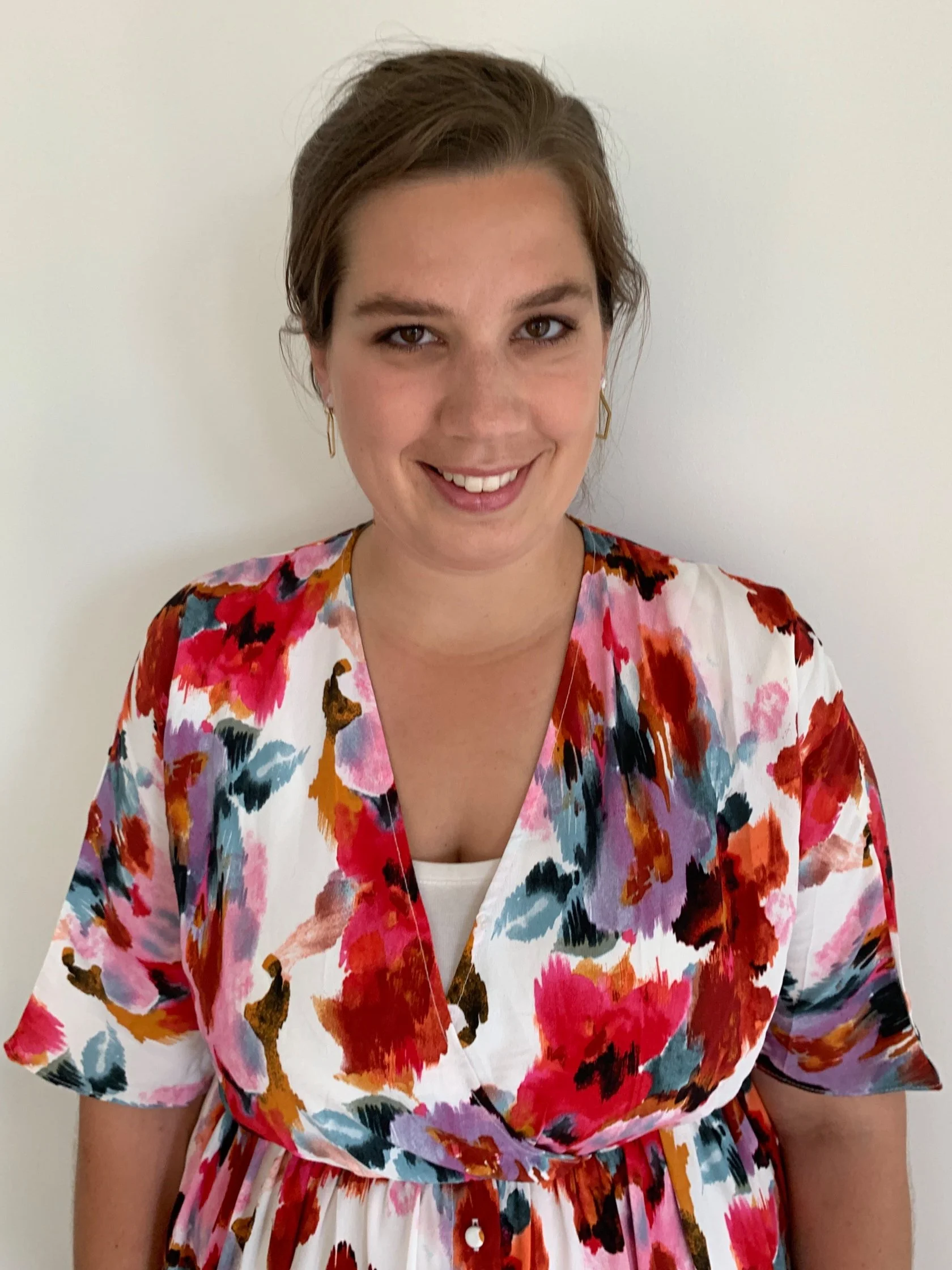 Person smiling, wearing a colorful floral dress against a white background.
