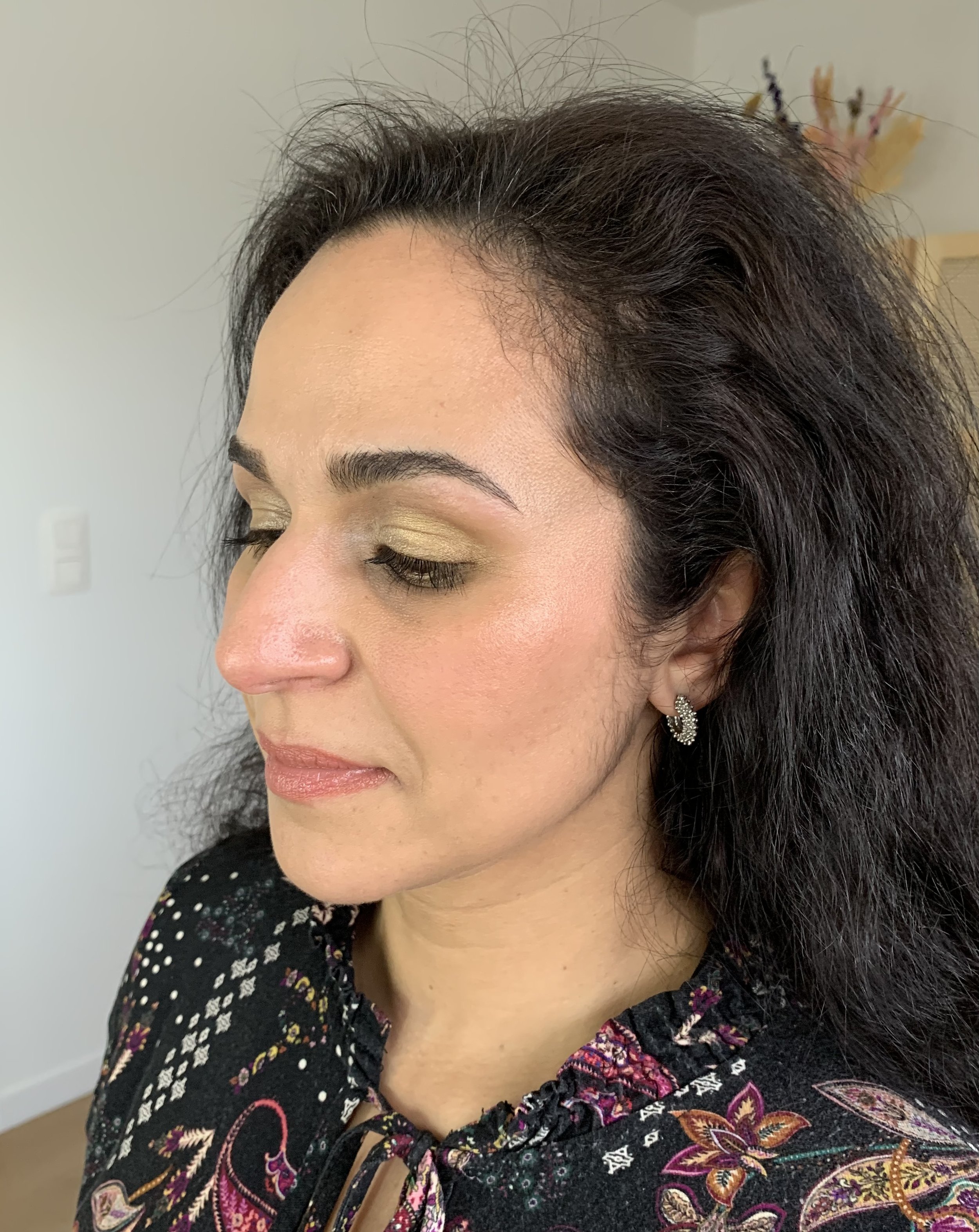 Woman with dark hair, wearing makeup and earrings, in a patterned blouse, side profile view.
