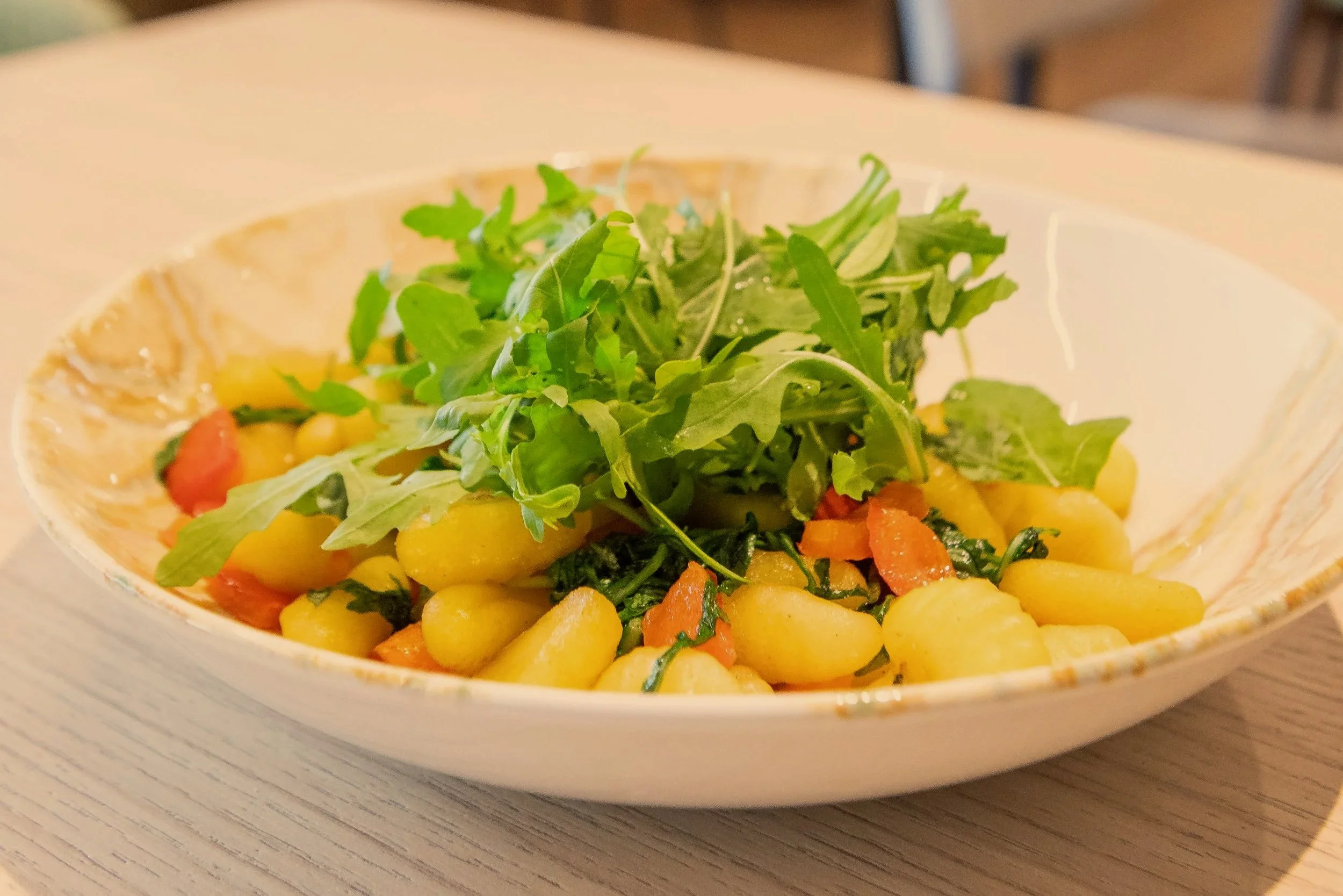 A bowl of gnocchi pasta with vegetables topped with fresh arugula and mixed greens.