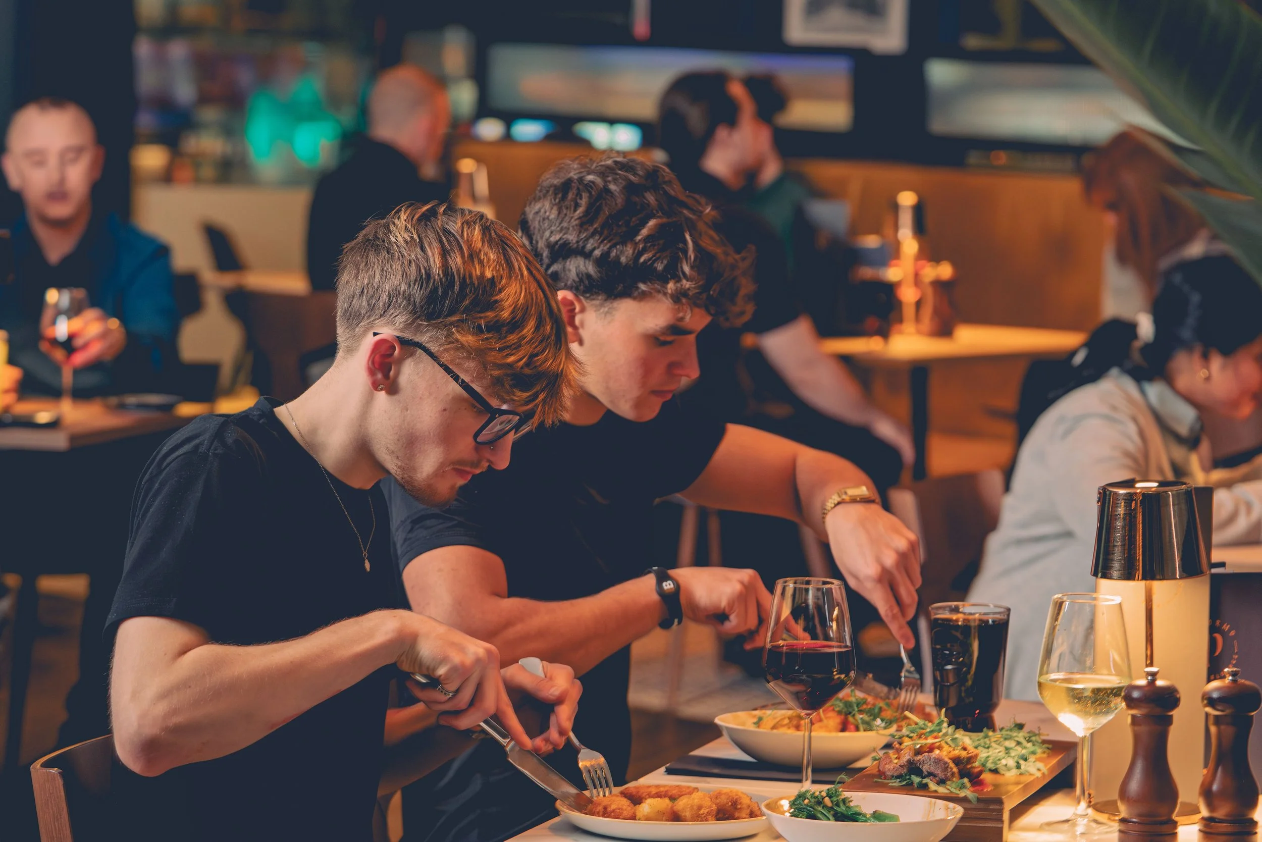 People having dinner at a restaurant with various dishes and drinks on the table.
