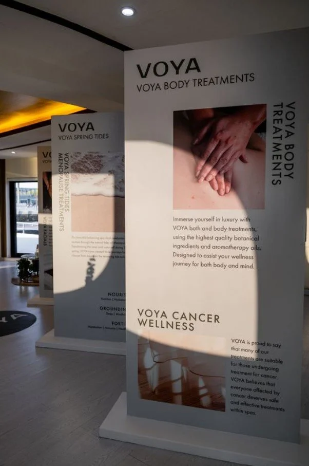Display boards advertising VOYA body treatments, including spring tides, cancer wellness, and aromatherapy, in a wellness center.