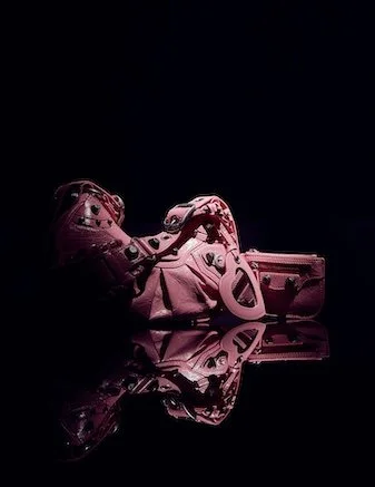 Pink football cleats with a matching pink purse reflected on a shiny black surface.