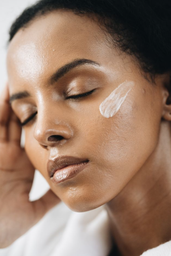 Close-up of a woman with closed eyes and a smear of white cream on her cheek, possibly skincare.