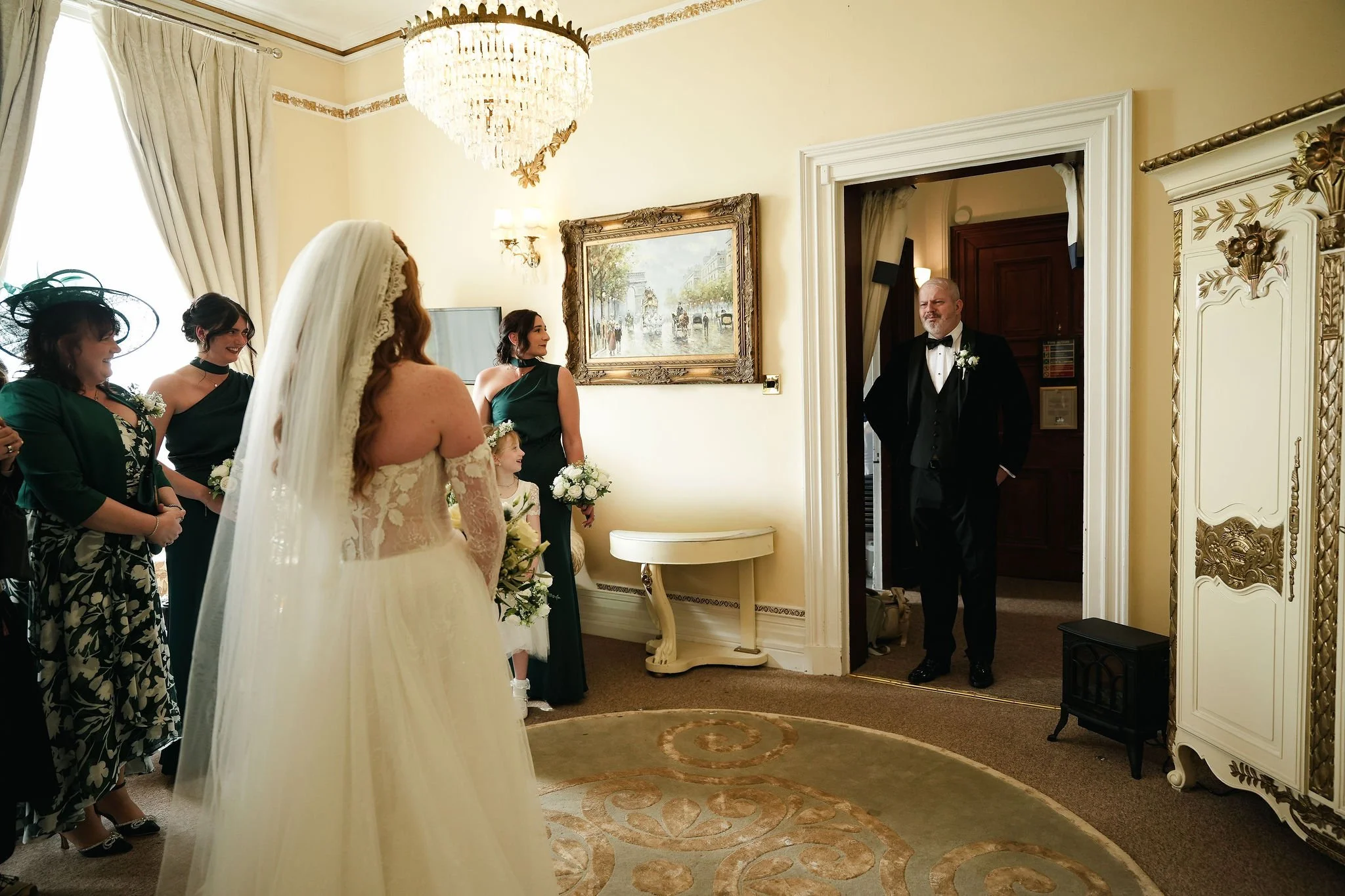A wedding ceremony in a decorated room with a bride, bridesmaids, and a groom.