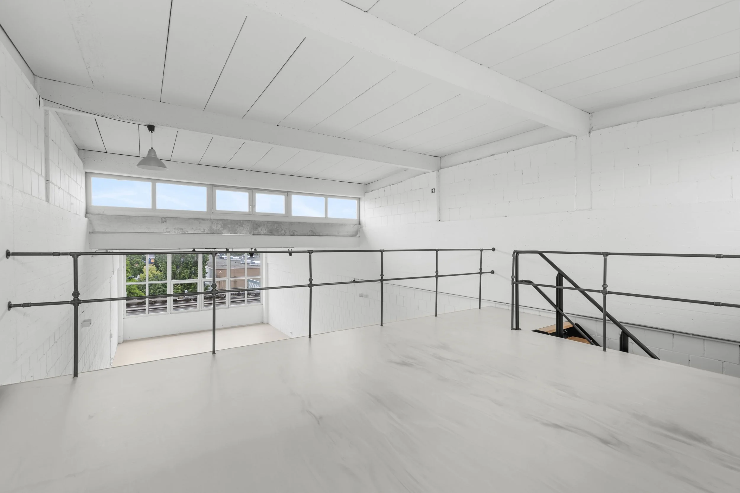 Innenraum eines weißen, modernen Gebäudes mit großen Fenstern, einer Treppe und Geländern aus schwarzem Metall.
