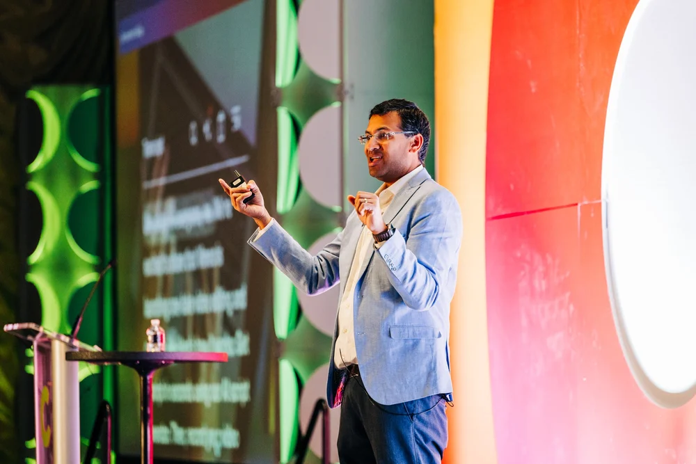 Birju Shah delivering a keynote on stage in front of a colourful backdrop