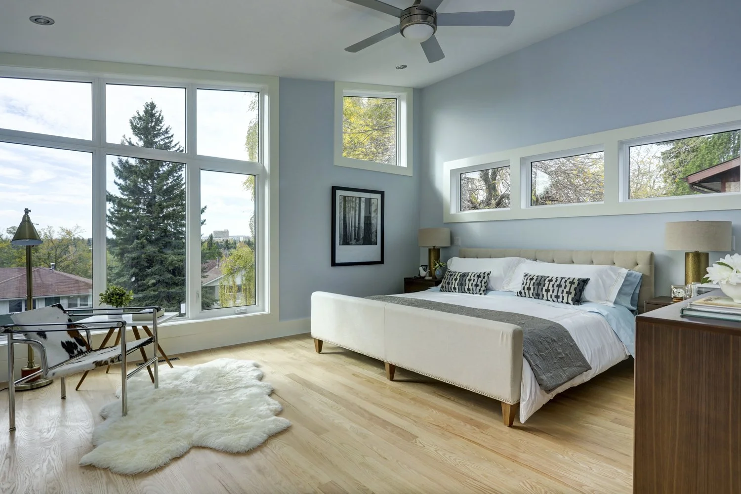 Bright bedroom with large windows, white and beige furniture, wooden floor, and minimalist decor.