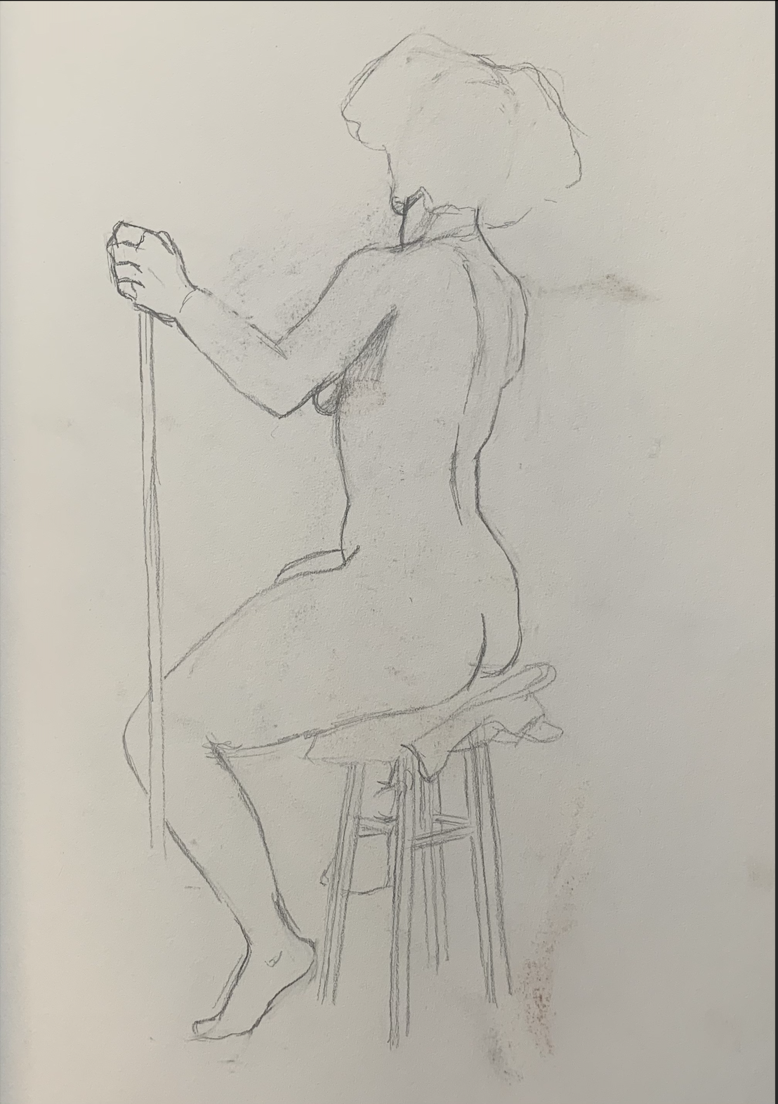 A pencil sketch of a nude woman sitting on a wooden stool, holding a long stick or rod, with short hair and her face turned slightly to the side.