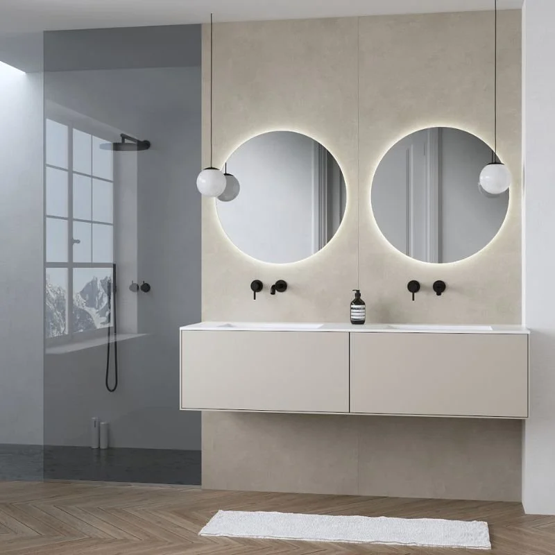 Modernes Badezimmer mit Doppelwaschbecken, runden Spiegeln mit Beleuchtung, schlichten schwarzen Wasserhähnen, einem Fenster mit Bergen im Hintergrund, einer Dusche mit Glaswand und einer weißen Teppich auf Holzboden.