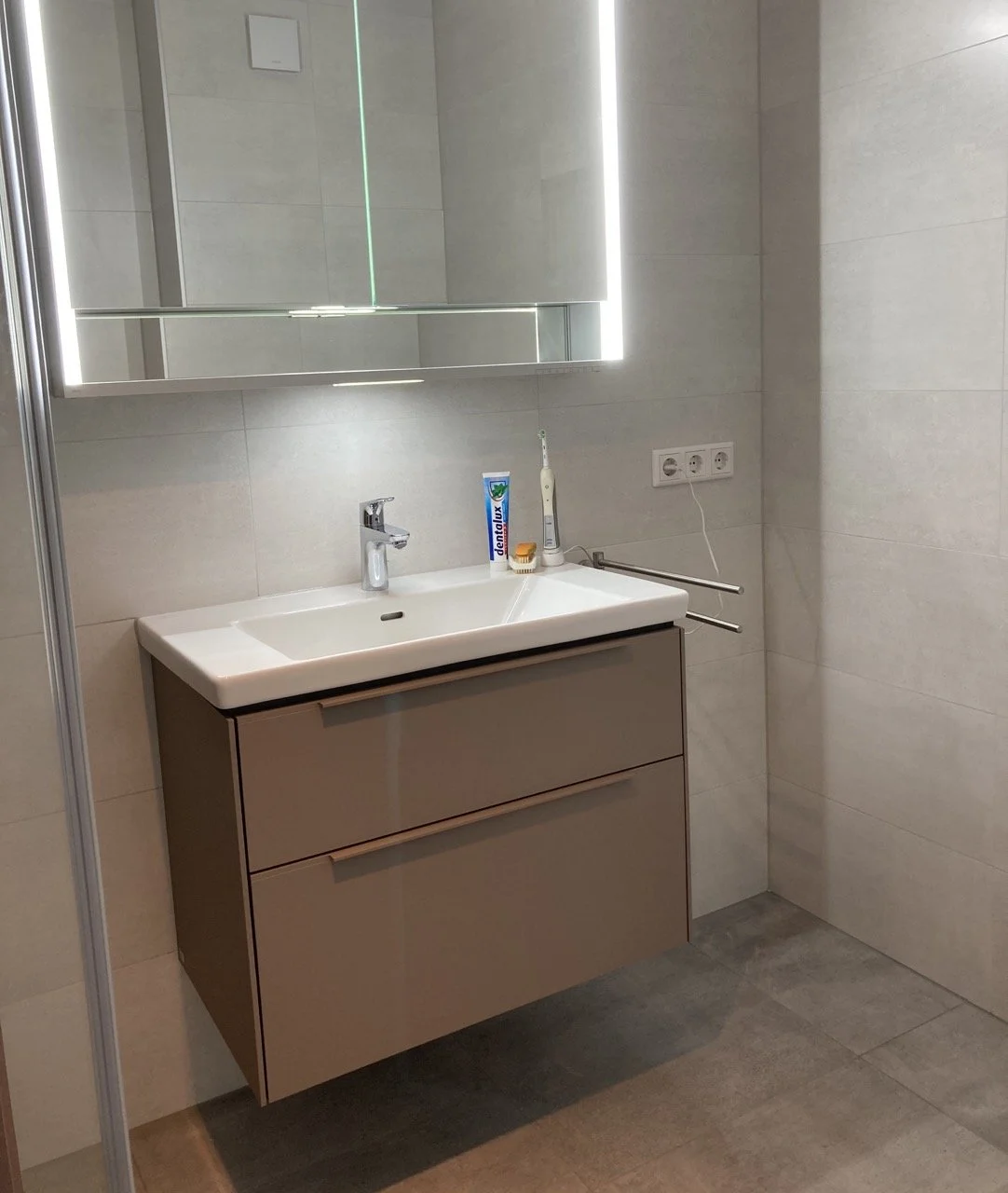 Waschbecken mit Spiegel, Zahnbürste, Zahnpasta und Steckdosen im Badezimmer.