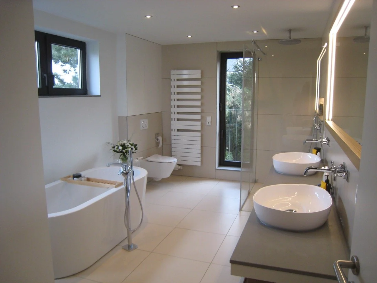 Modernes Badezimmer mit Doppelwaschbecken, Badewanne, Toilette, Heizkörper, Fenster und Tageslicht.