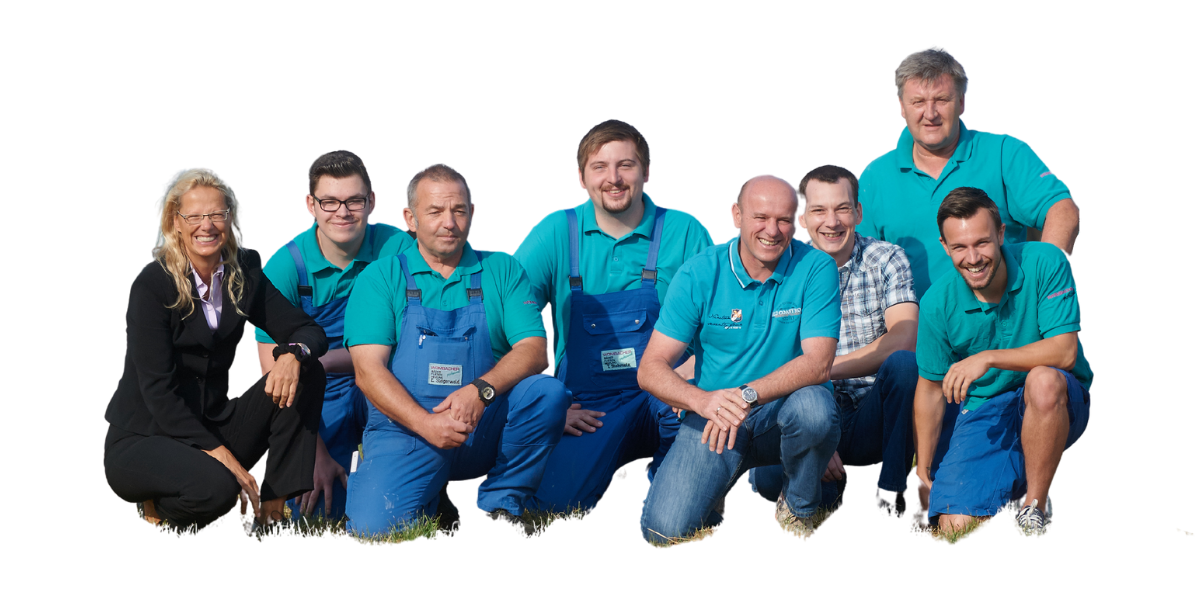 Eine Gruppe von acht Menschen, vermutlich Arbeiter, die draußen auf dem Rasen stehen und lachen, einige tragen blaue Arbeitskleidung.