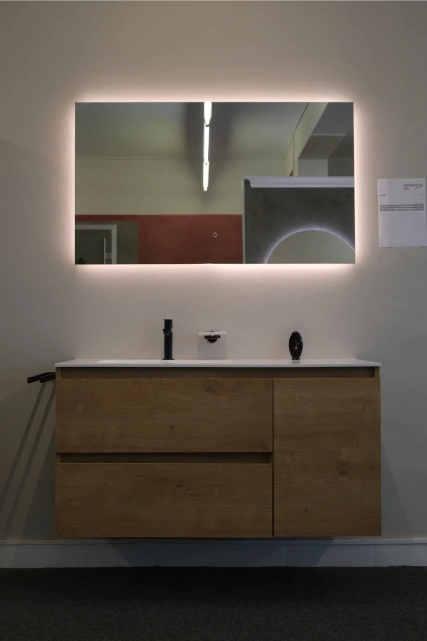 Moderner Holz-Waschtisch mit schwarzer Armatur, hinter einem beleuchteten Spiegel in einem minimalistischen Raum.