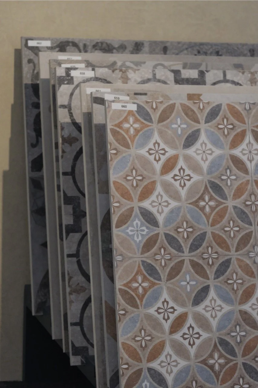 Mehrere Musterfliesen mit geometrischen Mustern in verschiedenen Farben, gelagert auf einem Regal.