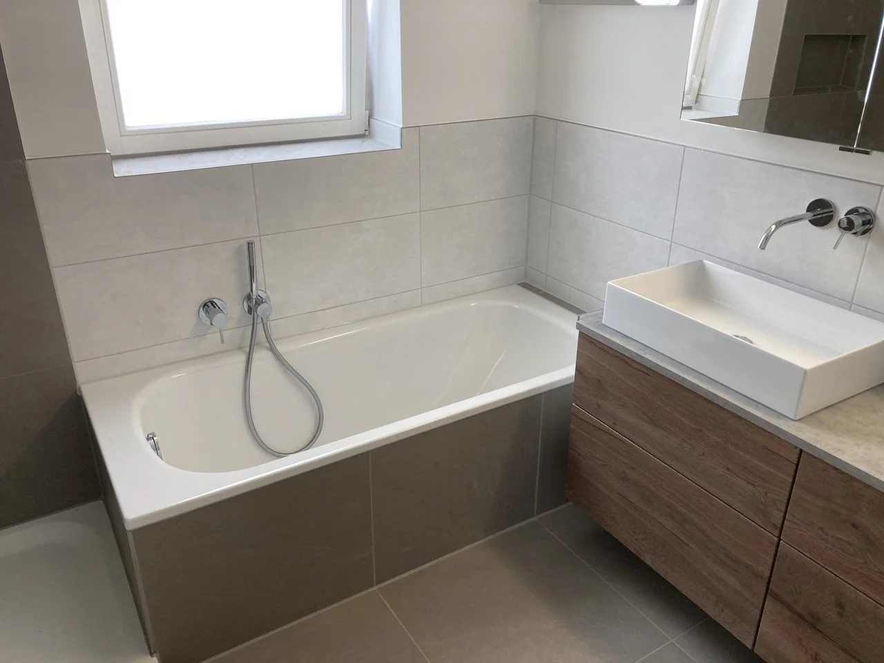 Modernes Badezimmer mit Badewanne, Waschbecken auf Holzschrank und Fenster.