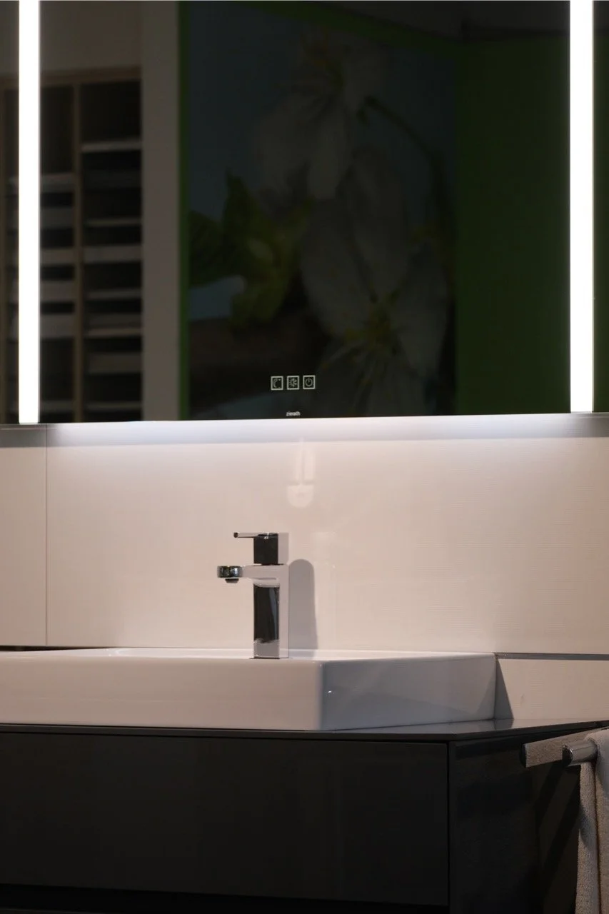 Waschbecken mit schwarzem Wasserhahn und großem Spiegel an der Wand, im Hintergrund ein Wandbild mit weißen Blumen auf grünem Hintergrund.