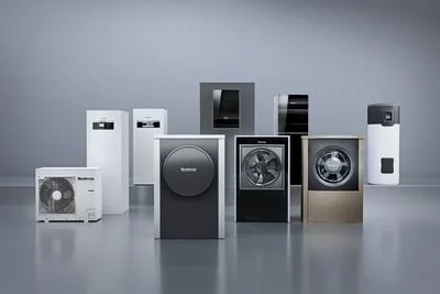 Verschiedene elektrische Haushaltsgeräte, hauptsächlich Waschmaschinen und Trockner, in einer Reihe auf einem grauen Hintergrund.