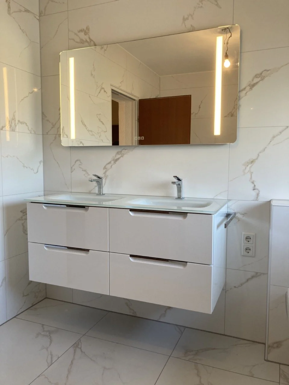 Moderner Doppelwaschtisch mit Spiegel und Beleuchtung im Badezimmer, weiße Verkleidung und Marmorfliesen.