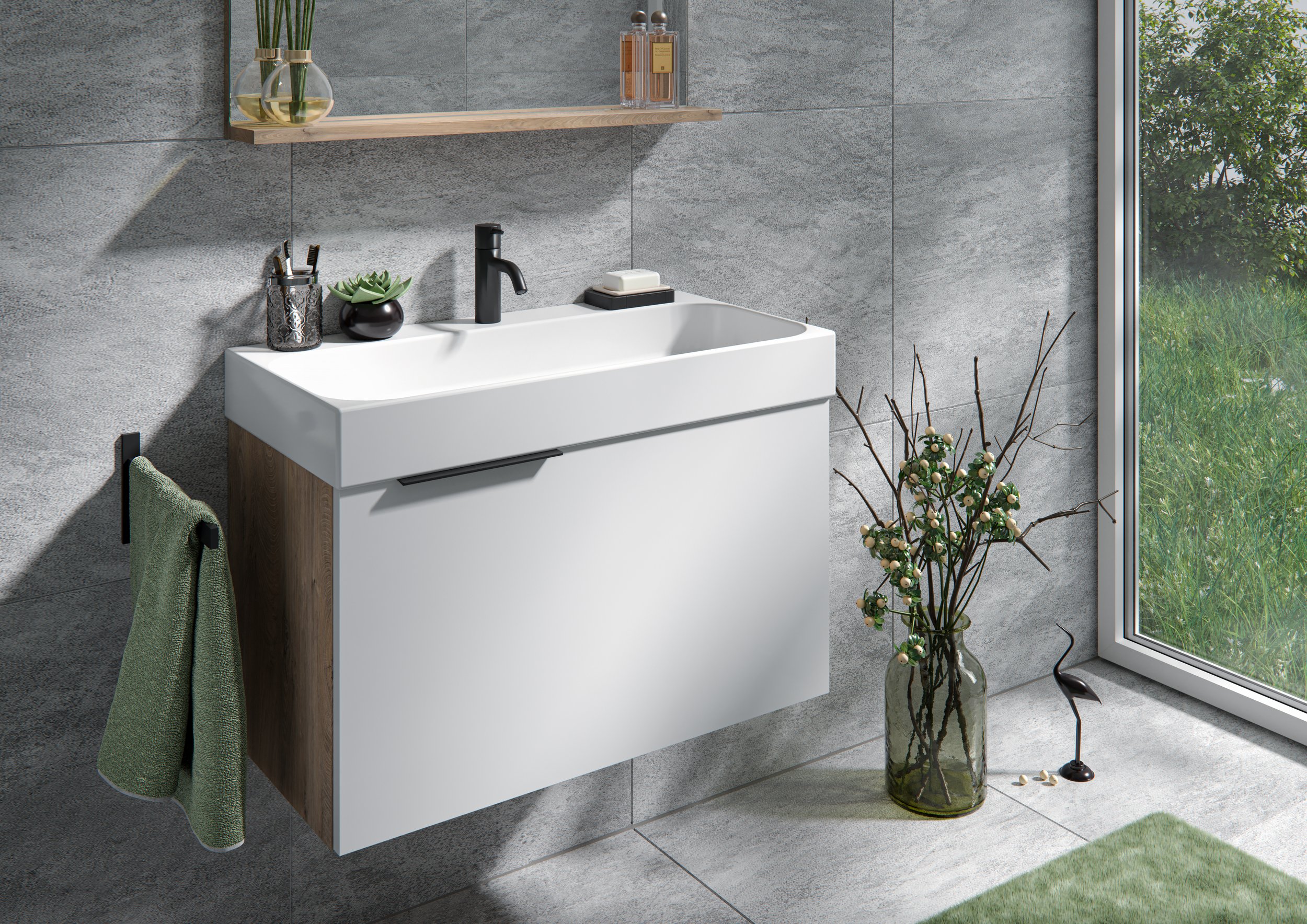 Moderner Badezimmerbereich mit grauen Wandfliesen, weißem Waschtisch mit schwarzem Wasserhahn und Holz seitlich. Es gibt einen grünen Handtuchhaken mit grünem Handtuch, eine Wandvase mit weißen Blüten, ein Regal mit Seifenspendern, und eine große Gla