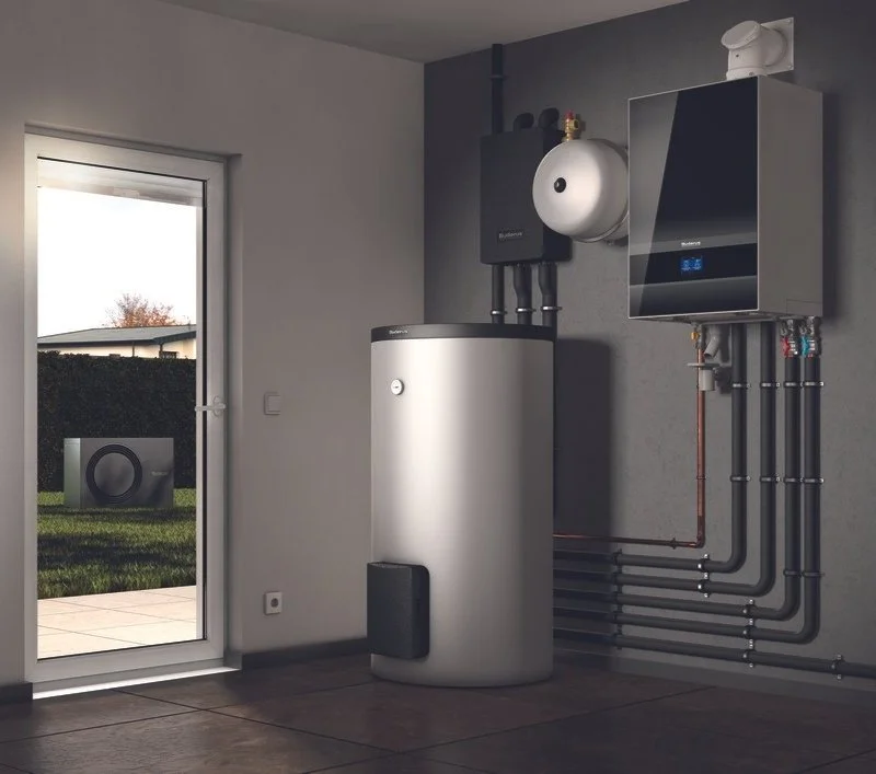 Innenraum mit einer Warmwasserenergieanlage, bestehend aus einem Wärmepumpenmodul, Pufferspeicher und Heizkreisverteilern, mit Blick nach draußen auf eine Garage.