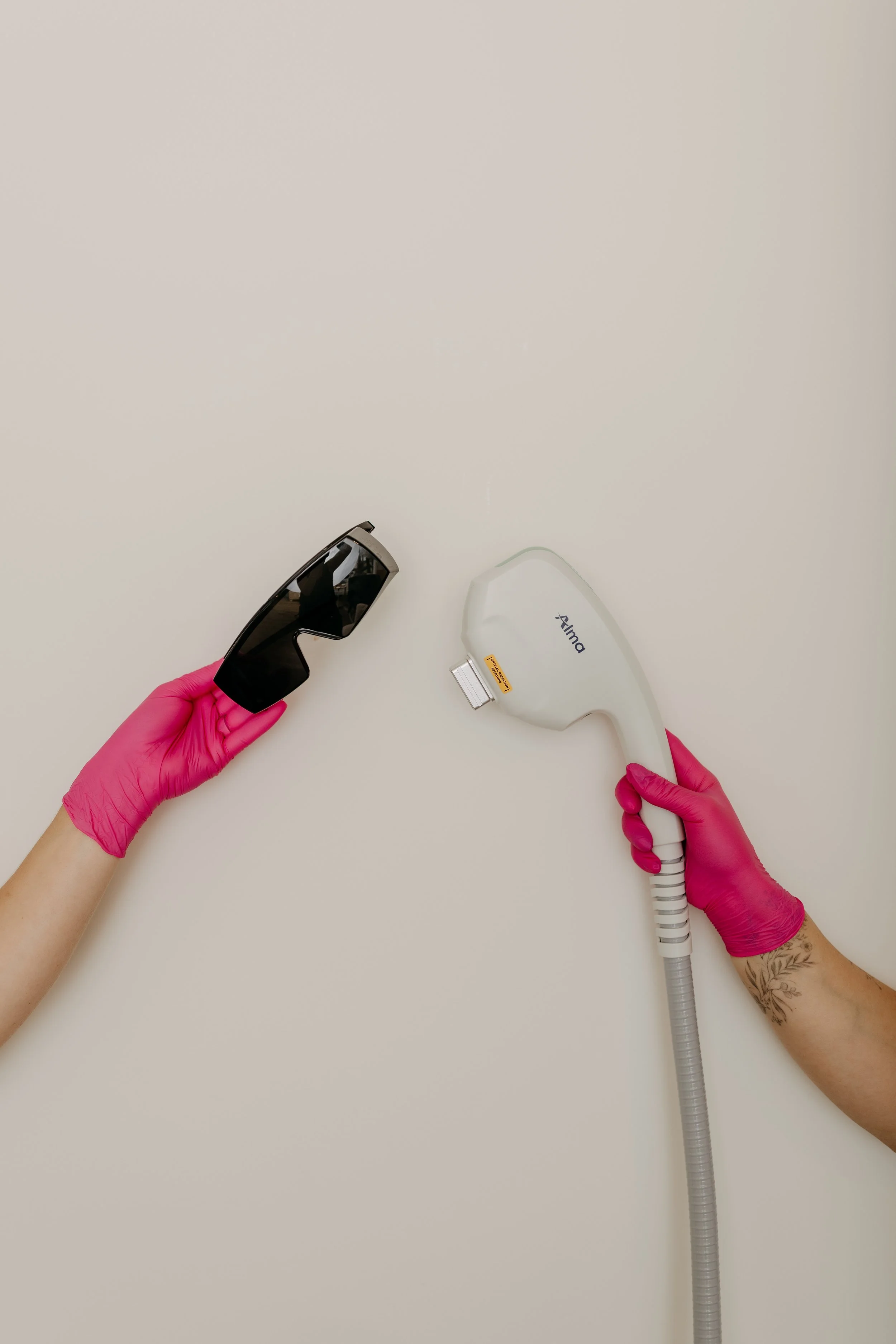 A person wearing pink gloves is holding a modern black handheld device with a reflective surface in one hand and a white handheld device marked 'Harmony' in the other hand on a plain white background.