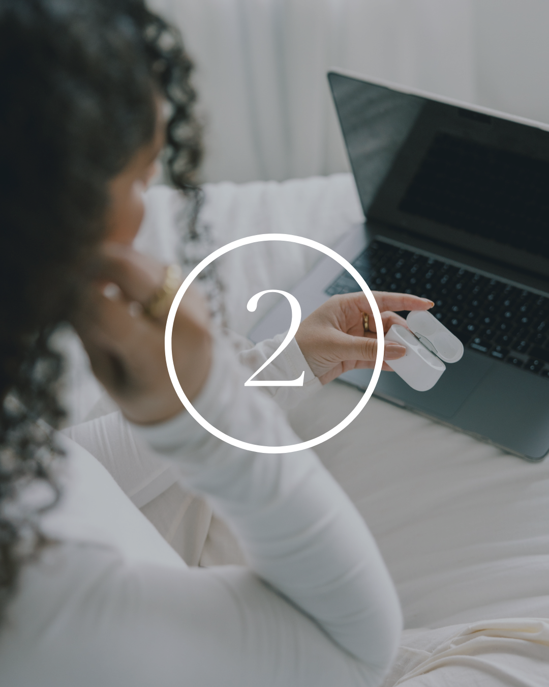 A woman sitting with a laptop on her lap, holding a wireless mouse in her right hand.