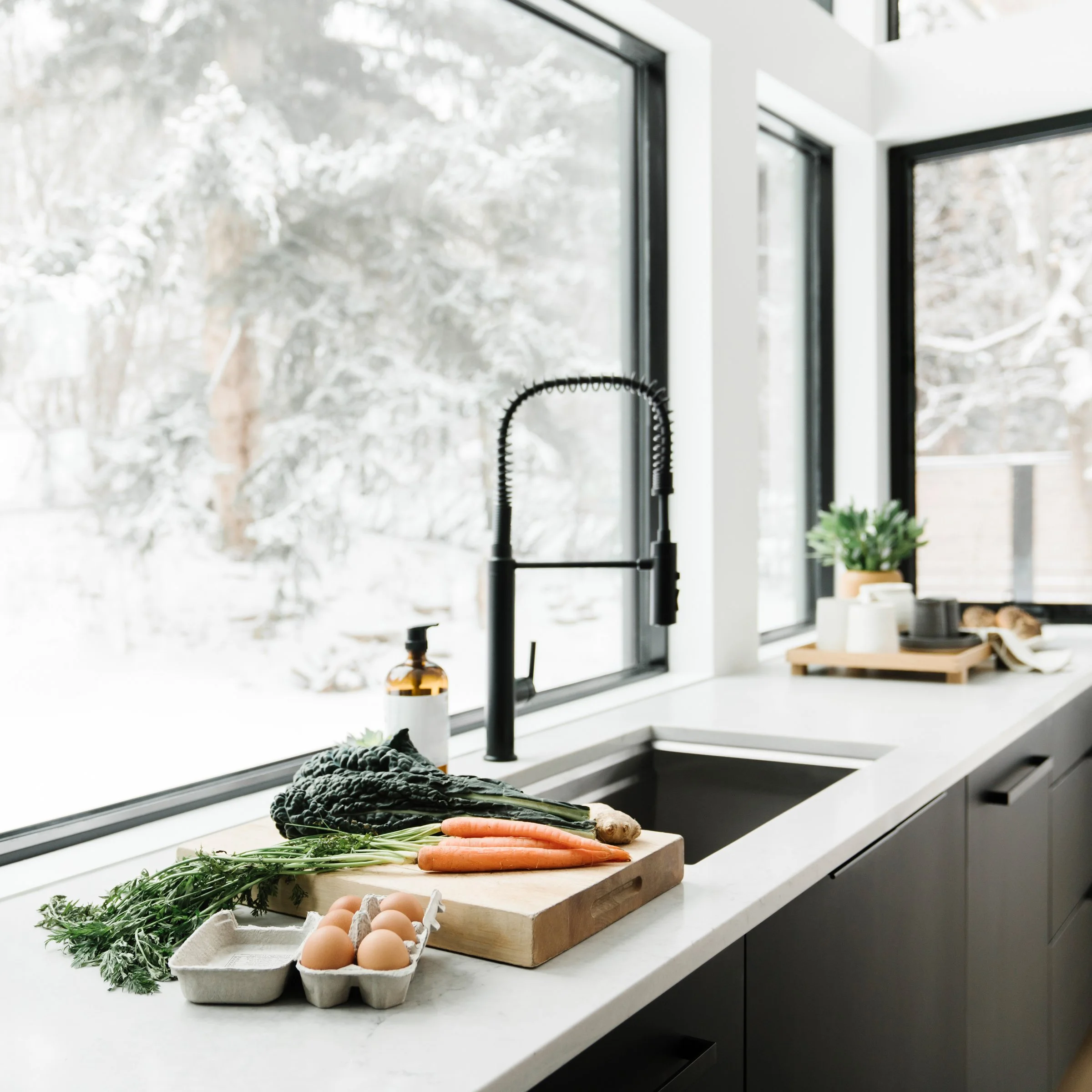 Kitchen counter with fresh vegetables, eggs, and kitchen supplies near a large window with a snowy outdoor scene.
