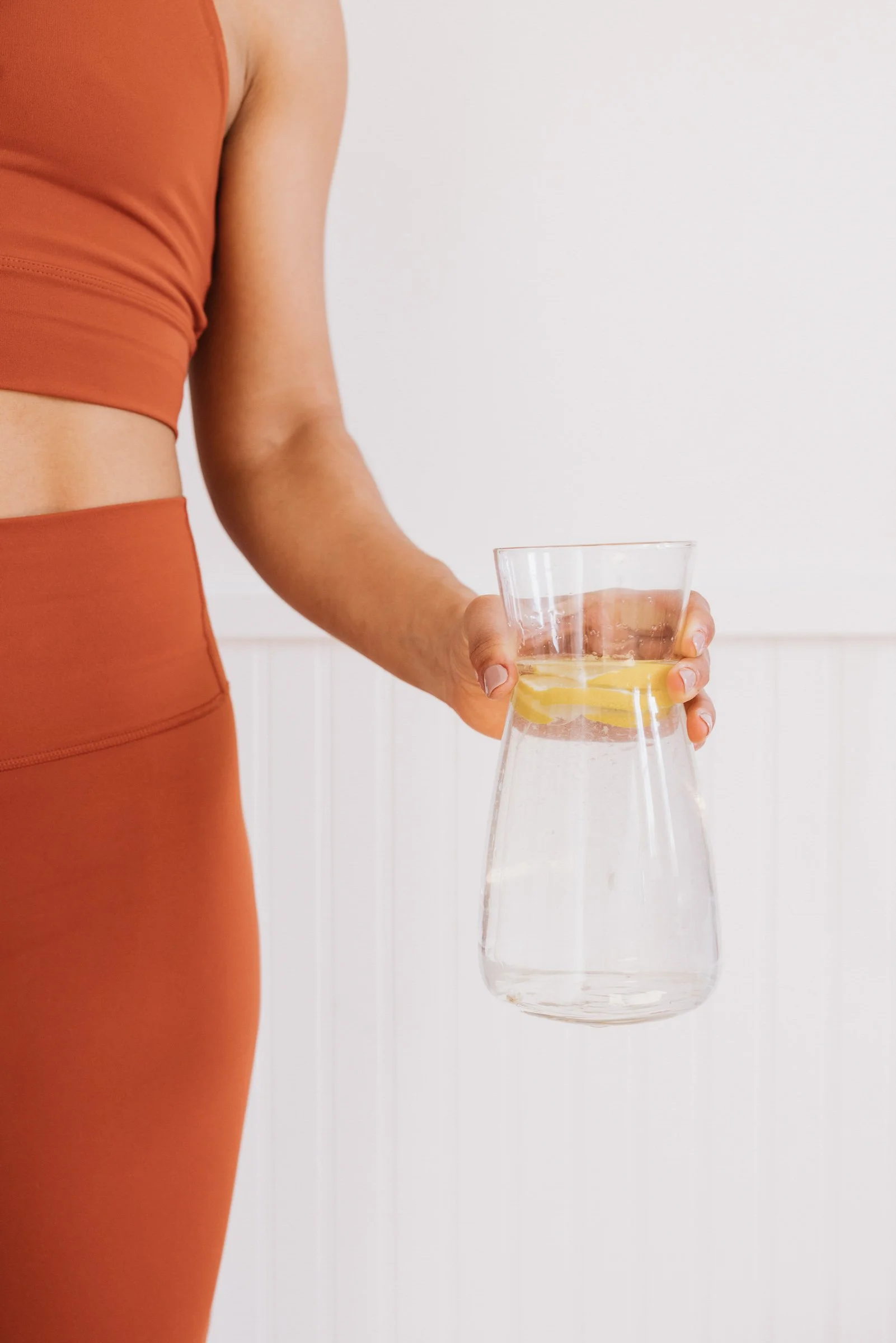 Person in orange athletic wear holding a glass pitcher with water and lemon slices.