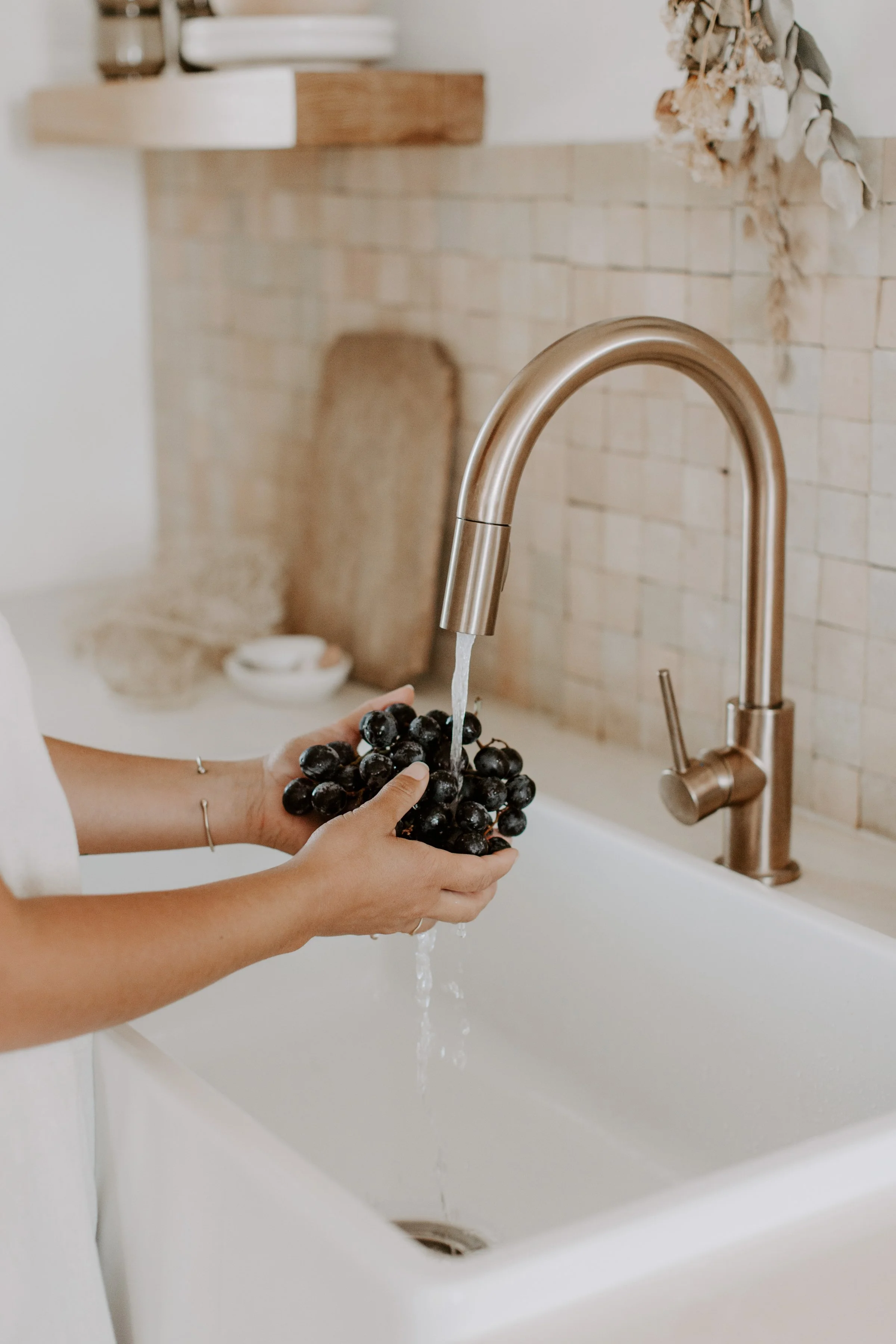 Person rinsing black grapes under a kitchen faucet in a modern kitchen.